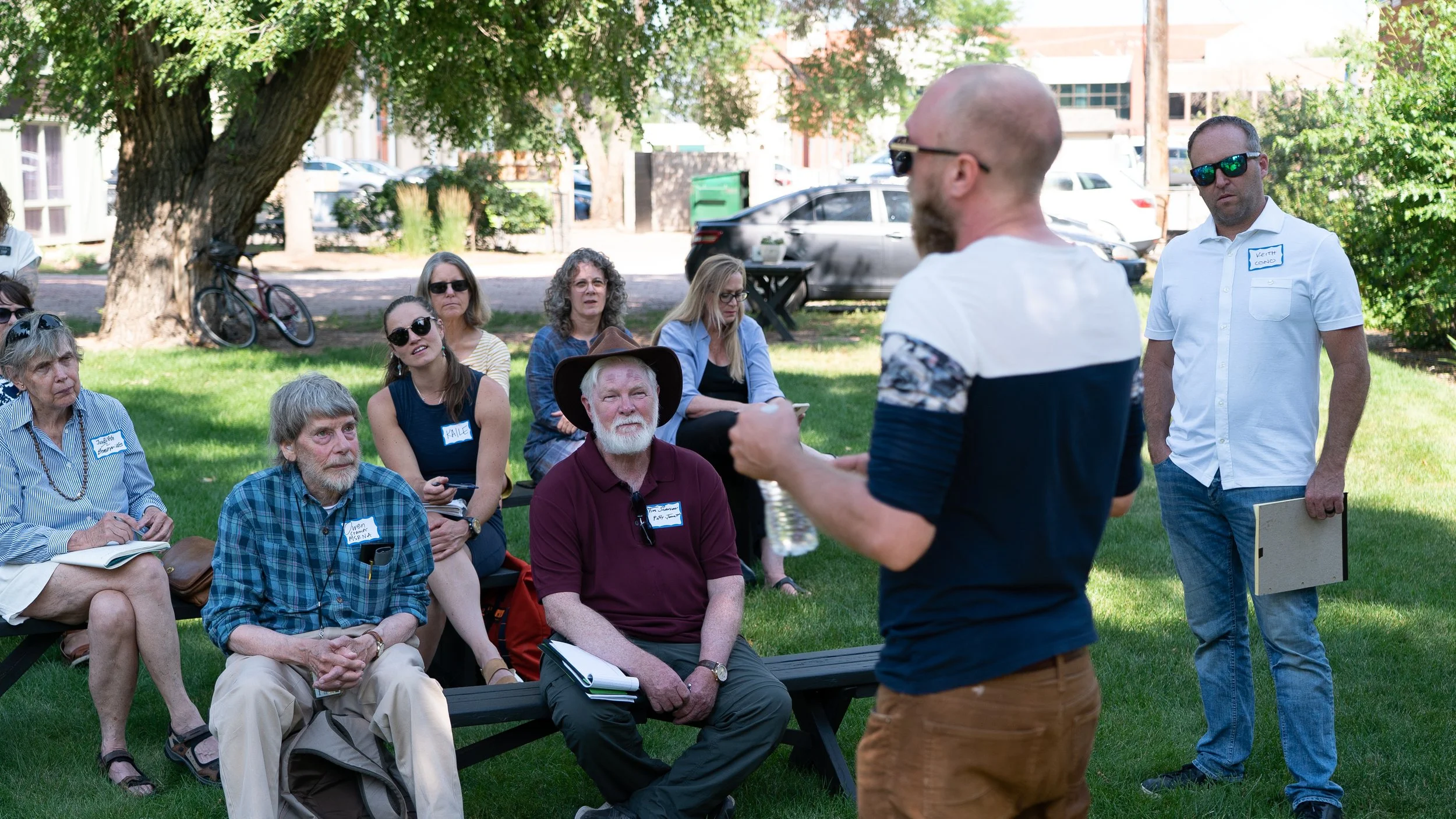 Outdoor meeting with people listening to a speaker in a park.