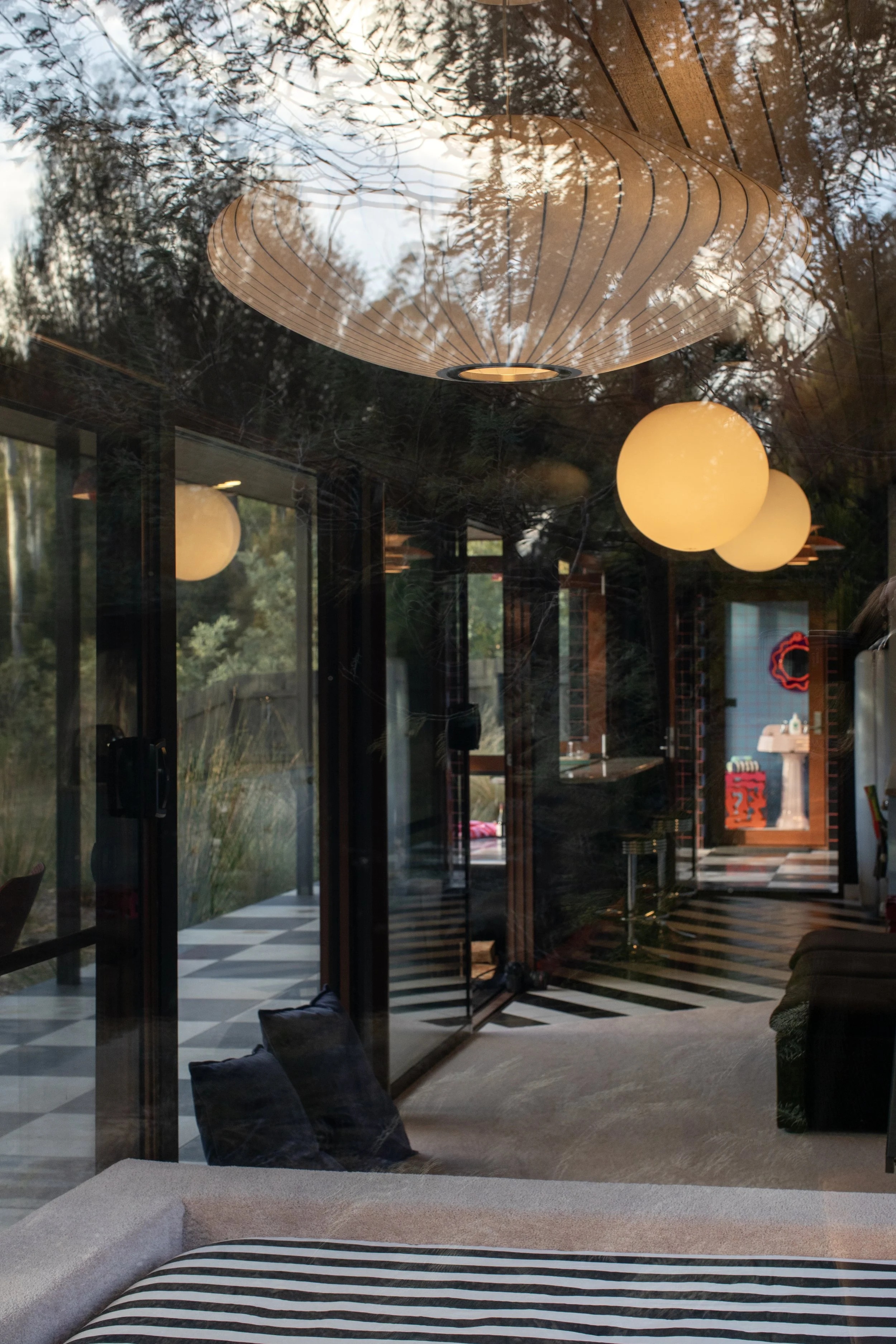 View through a glass window showing a modern interior with hanging pendant lights, a black and white checkered floor, and a glimpse of a room with furniture and decorations outside.