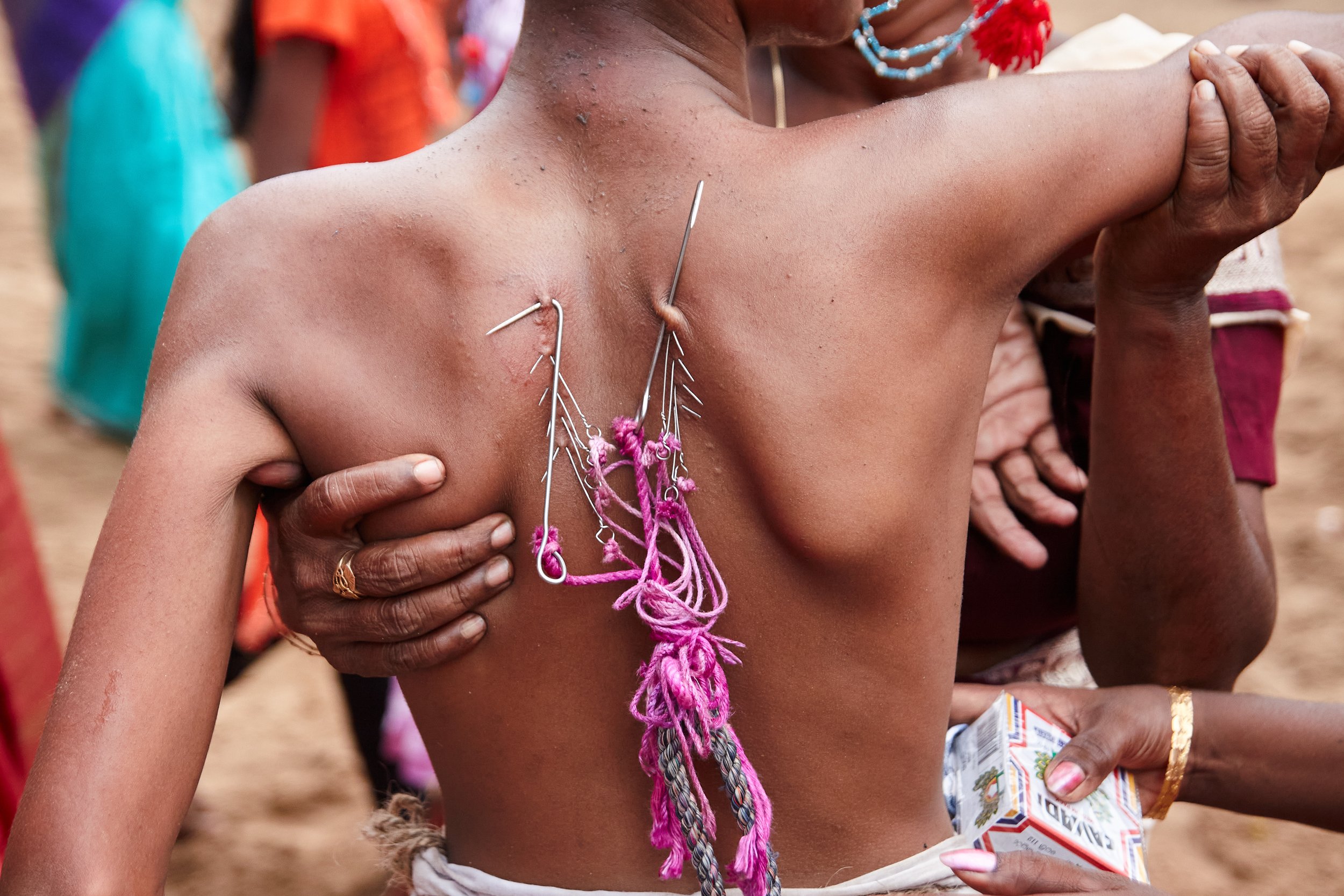 A family is holding a tired teenager during one of his ritual dance performances for the day. Sharp hooks are attached to the back, and the ropes help the bystander control the dancer during the heights of his performance. Several thousand devotees p