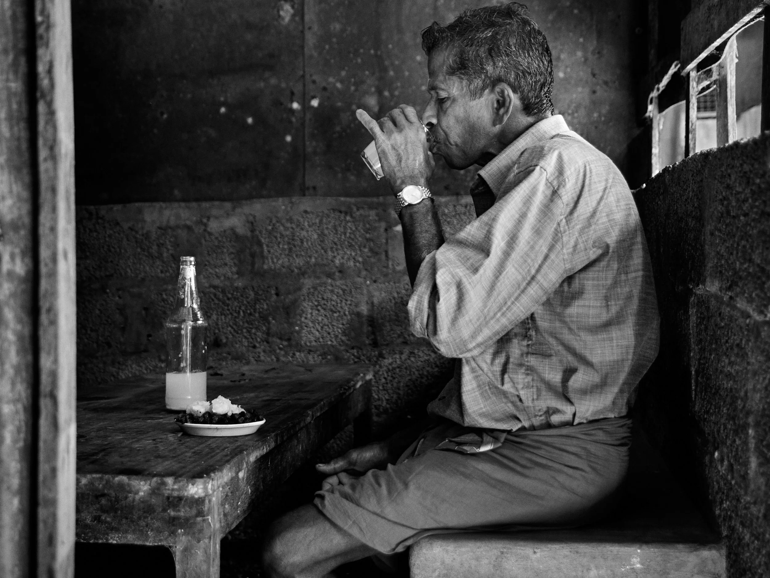 A villager enjoying a bottle of fresh toddy at a waterfront toddy shop.
