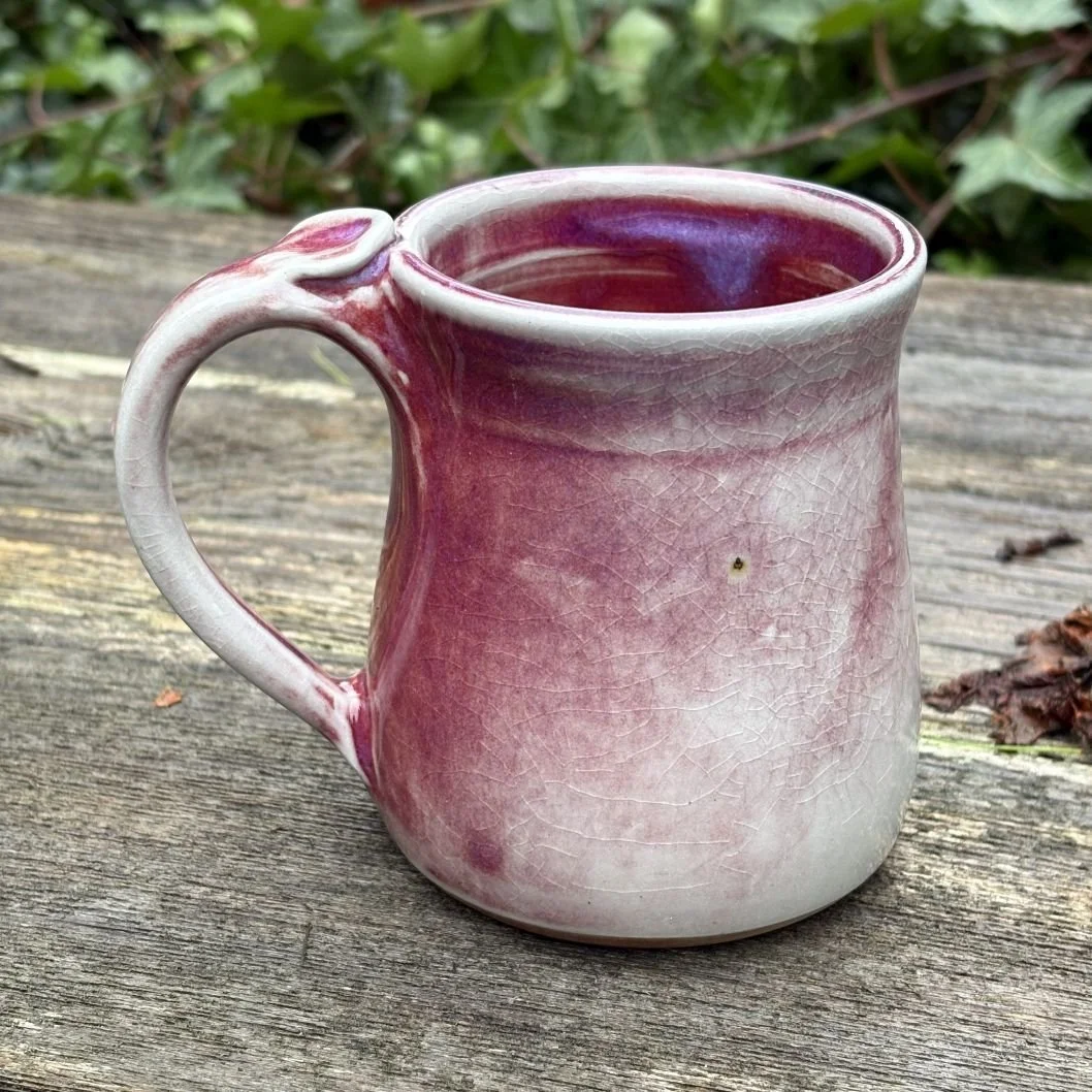 handmade ceramic mug with a deep wine-toned glaze fading into a pale greenish, lightly crackled base and a rounded pulled handle