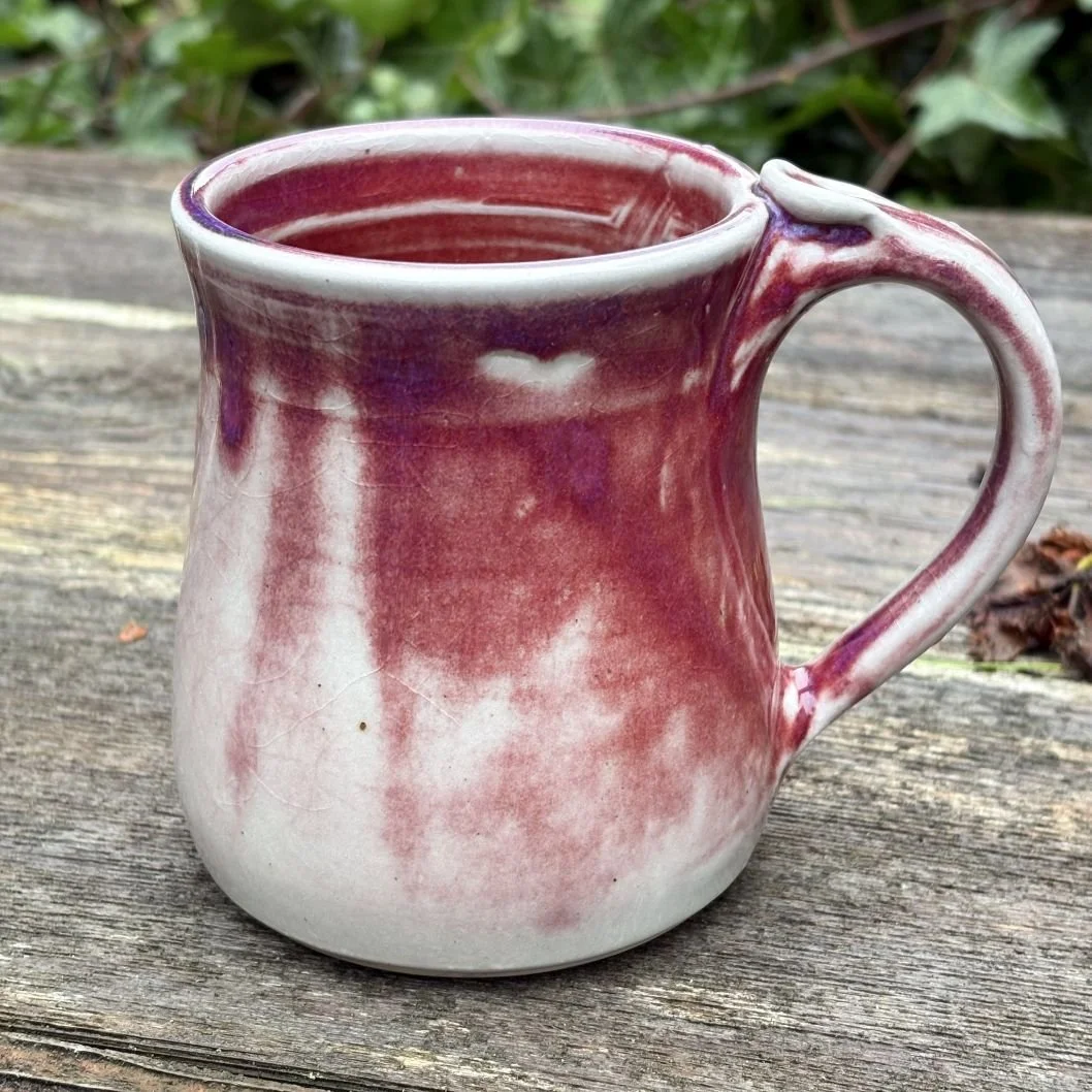 side view of handmade ceramic mug with a deep wine-toned glaze fading into a pale greenish, lightly crackled base and a rounded pulled handle
