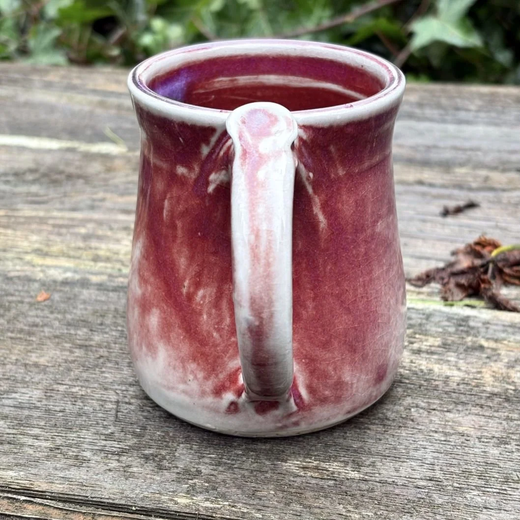 back view of handmade ceramic mug with a deep wine-toned glaze fading into a pale greenish, lightly crackled base and a rounded pulled handle
