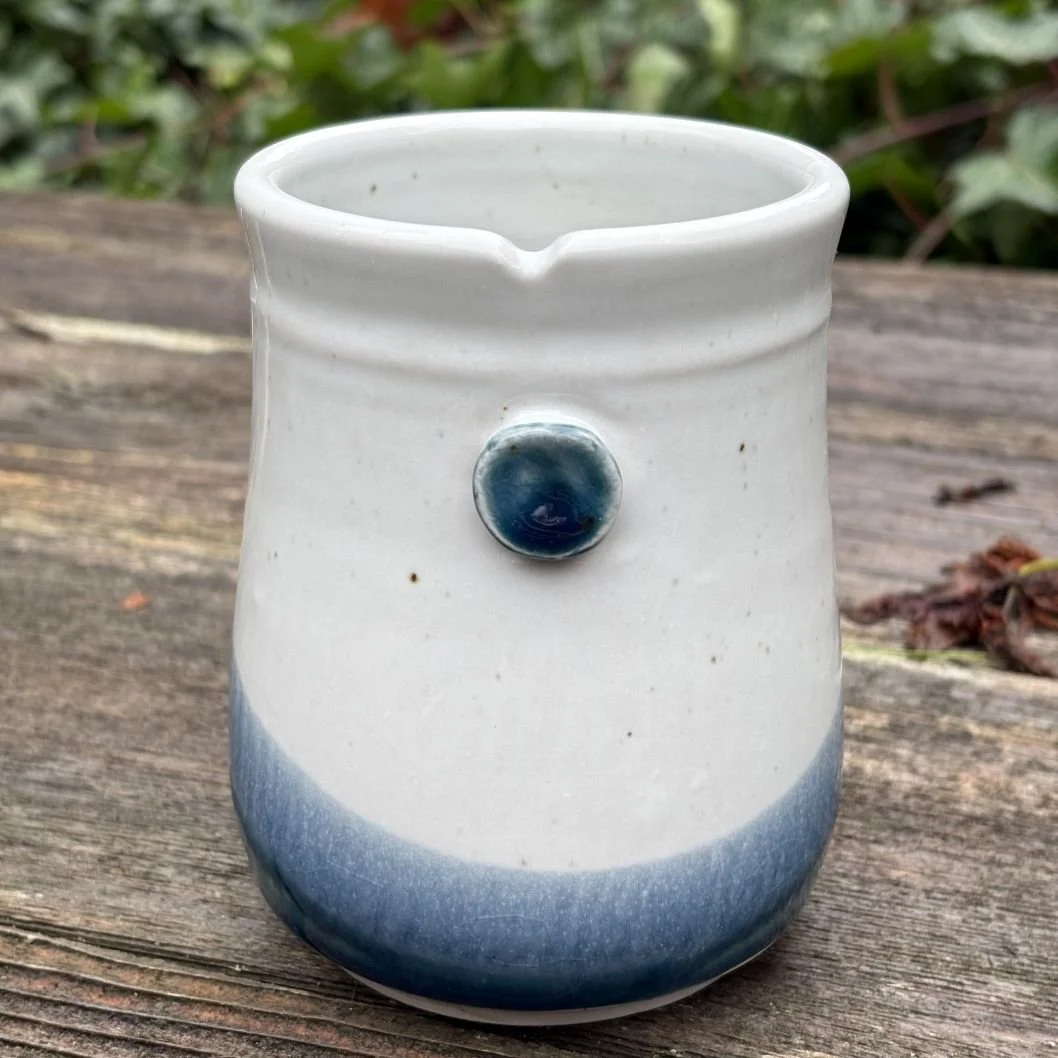 White ceramic mug with a blue gradient base and a small raised blue dot on its side, serving as a tie holder for tea bags.