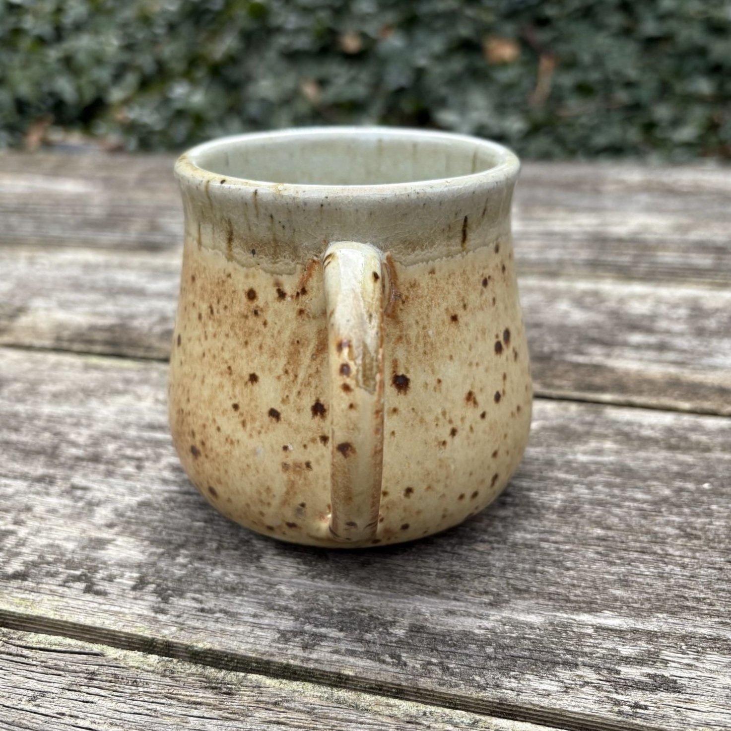Back profile view of mug, speckled yellow glazing on the outside with a white glazed rim, sits on a fence post.