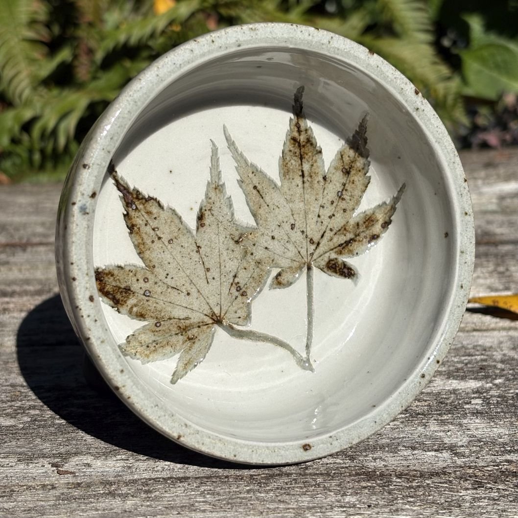 Two maple leaves imprinted in a dark clay bowl, covered with white ceramic slip, with clear glazing.