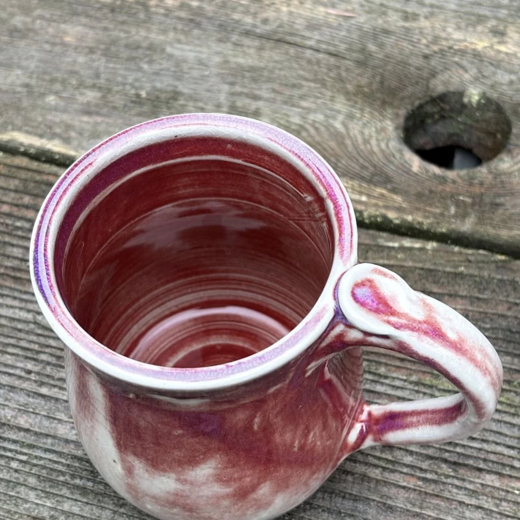 overhead view of handmade ceramic mug with a deep wine-toned glaze fading into a pale greenish, lightly crackled base and a rounded pulled handle