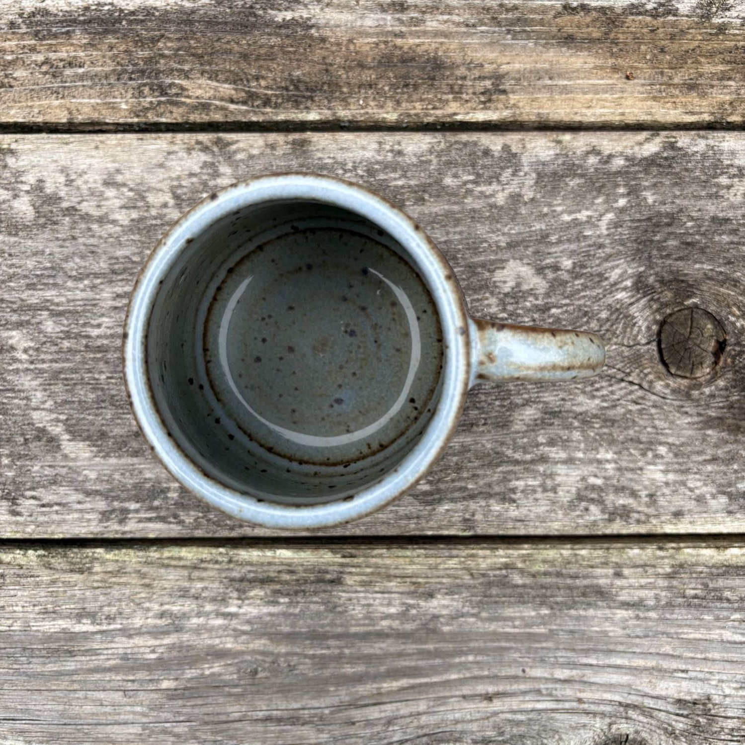 Overhead view of mug sitting on rustic fence panel, showing rich cornflower blue glazed interior and top of mug handle.