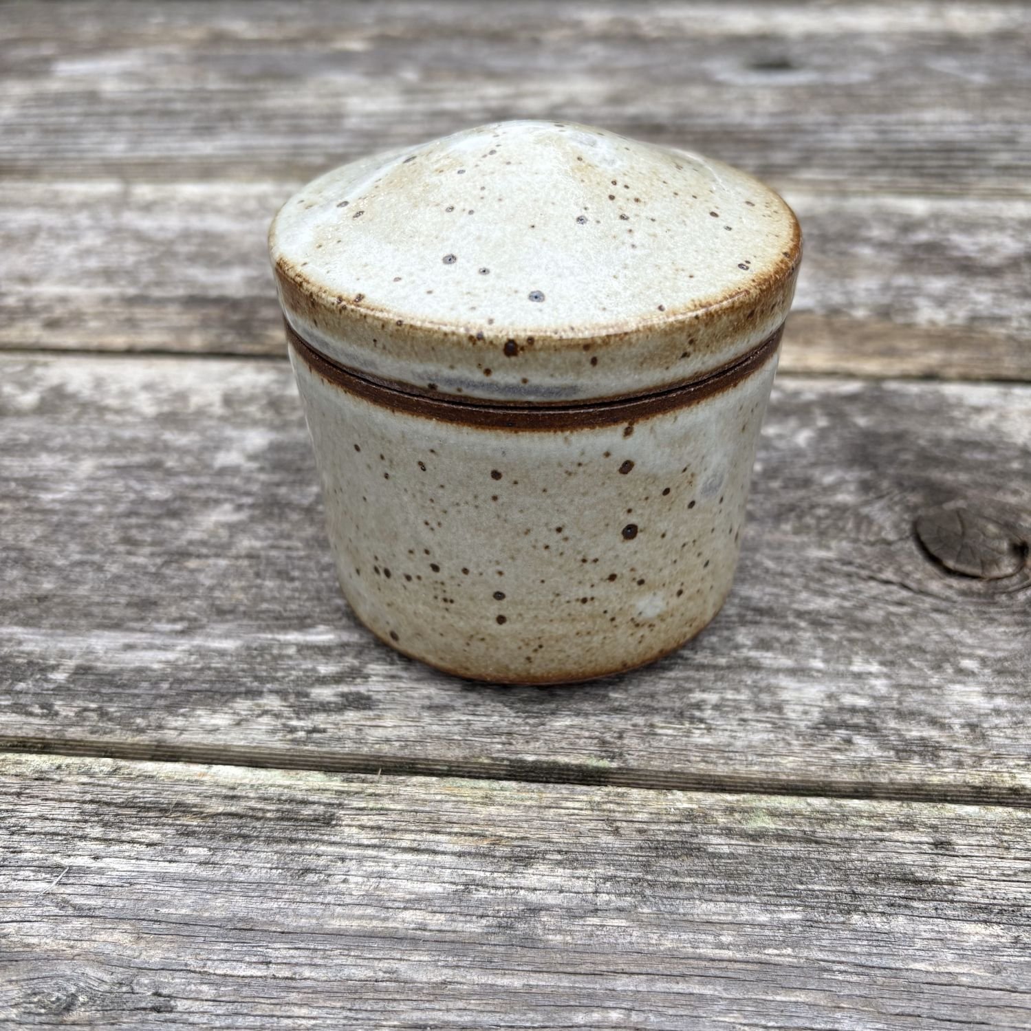 Jar, with lid on, both are glazed in satin white on dark clay with speckling. Gray lines of carbon-trapping seen on edge of jar lid.