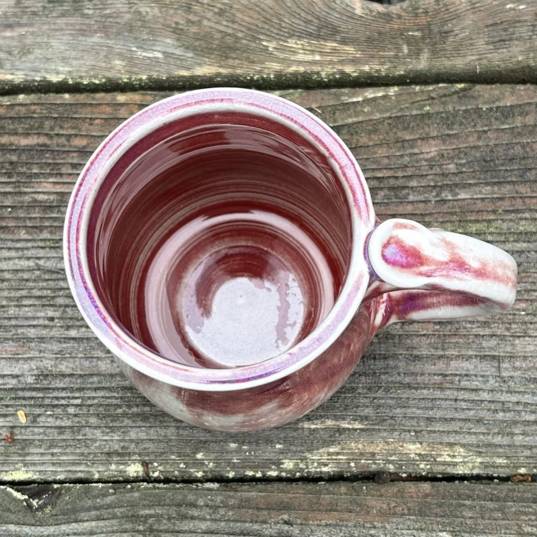 overhead view of handmade ceramic mug with a deep wine-toned glaze fading into a pale greenish, lightly crackled base and a rounded pulled handle