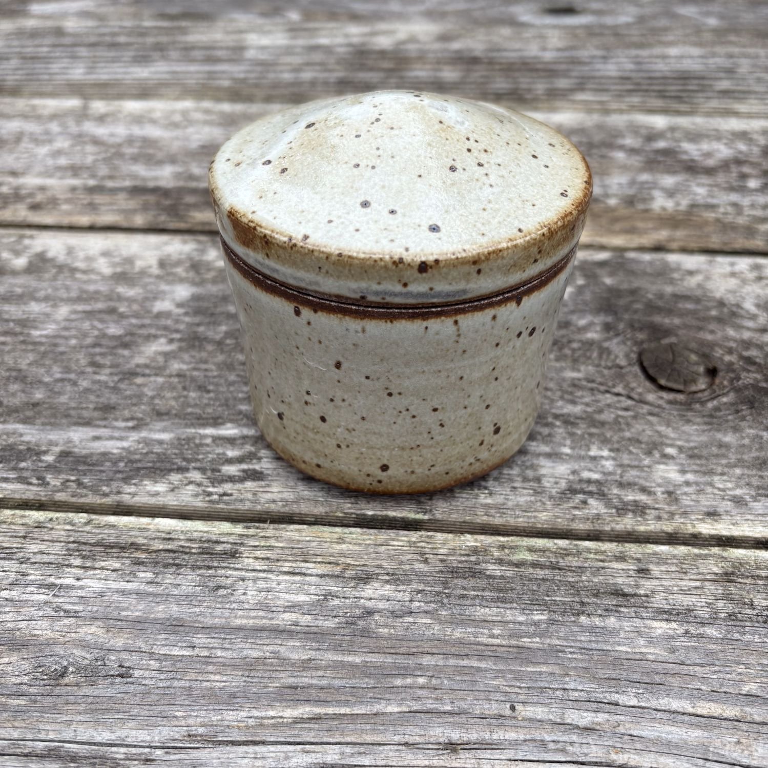 Jar, with lid on, both are glazed in satin white on dark clay with speckling. Gray lines of carbon-trapping seen on edge of jar lid.