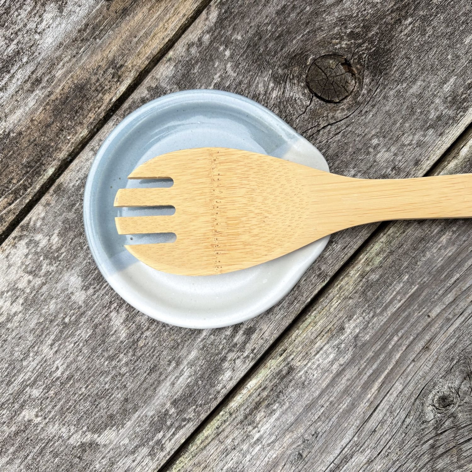 Overhead view of white and cornflower blue spoon rest on aged fence, highlighting the contrast between the dish and the aged fence.