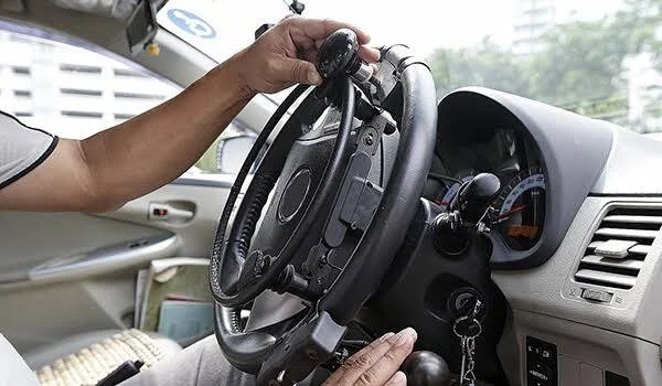 Person sitting in driver's seat adjusting the steering wheel of a car with a view of the dashboard and cityscape through the window.