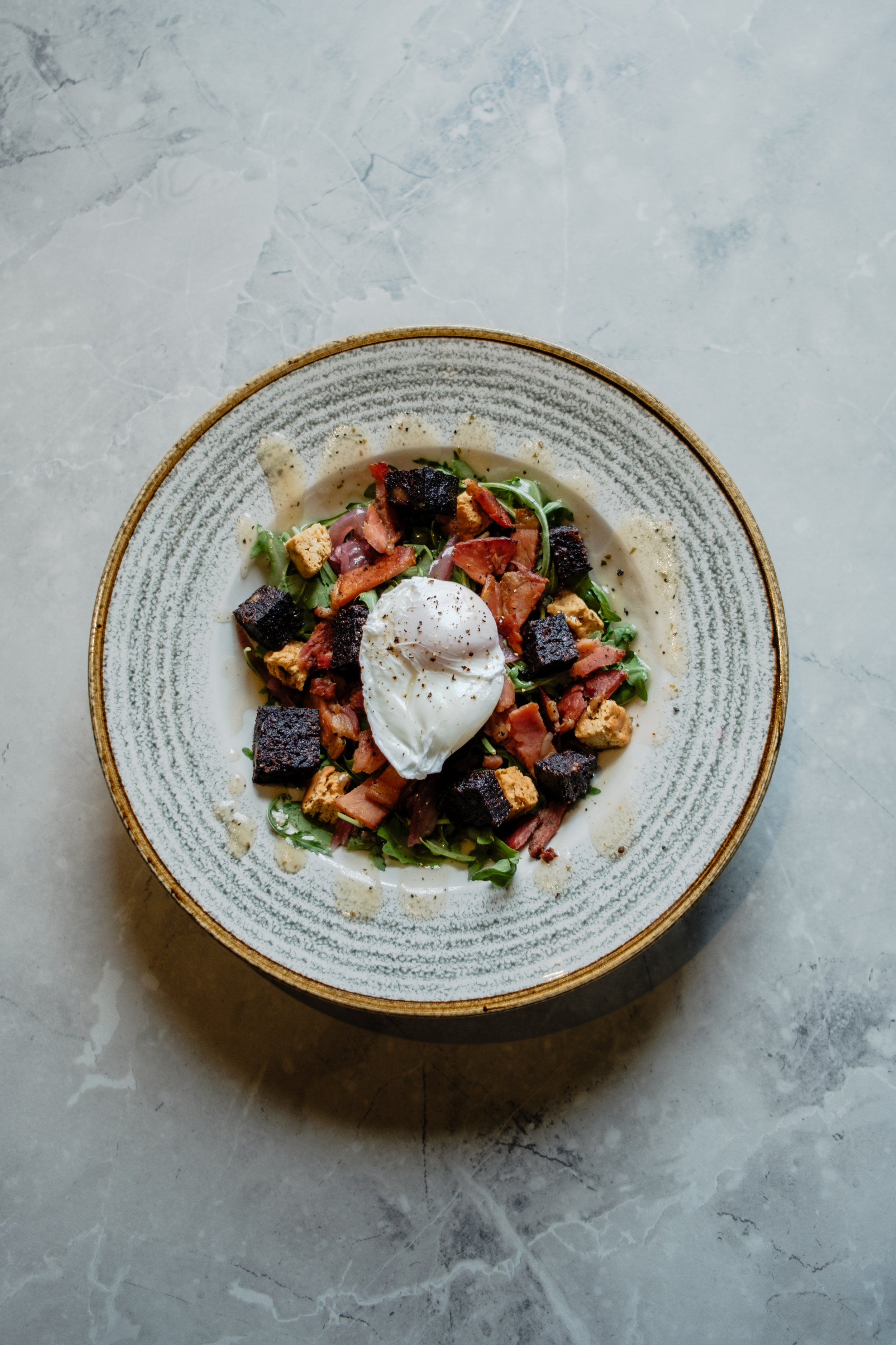 A salad with bacon, croutons, and a poached egg on top, served on a patterned ceramic plate.
