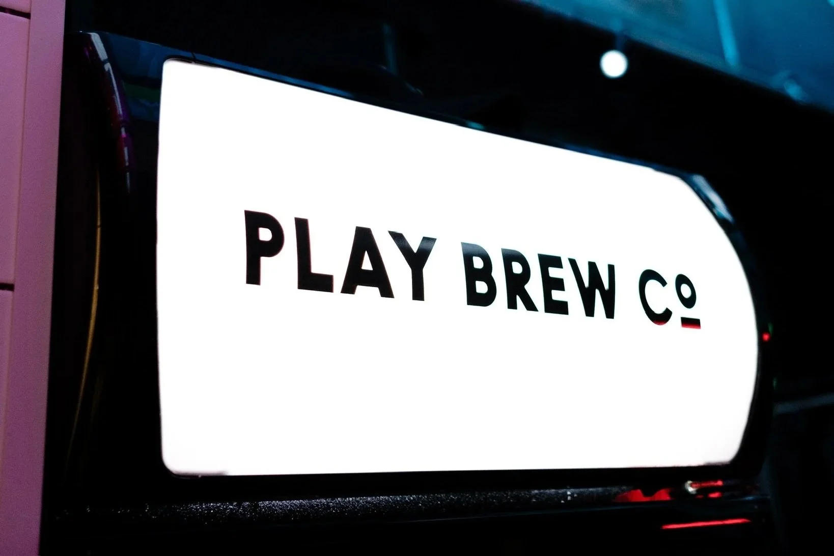 A digital sign displaying 'PLAY BREW CO' with a disco ball hanging above it in a dimly lit setting.