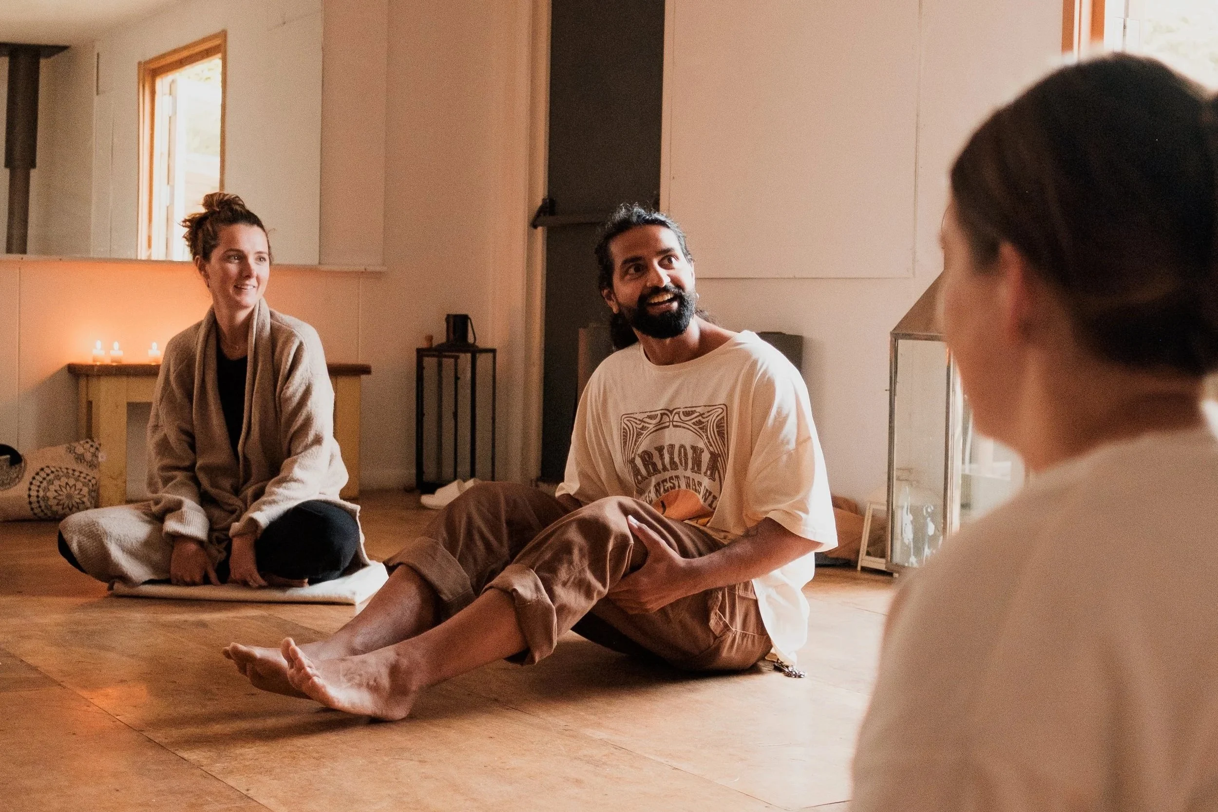 Four people sitting on the floor in a cozy, softly lit room, engaging in conversation and relaxation.