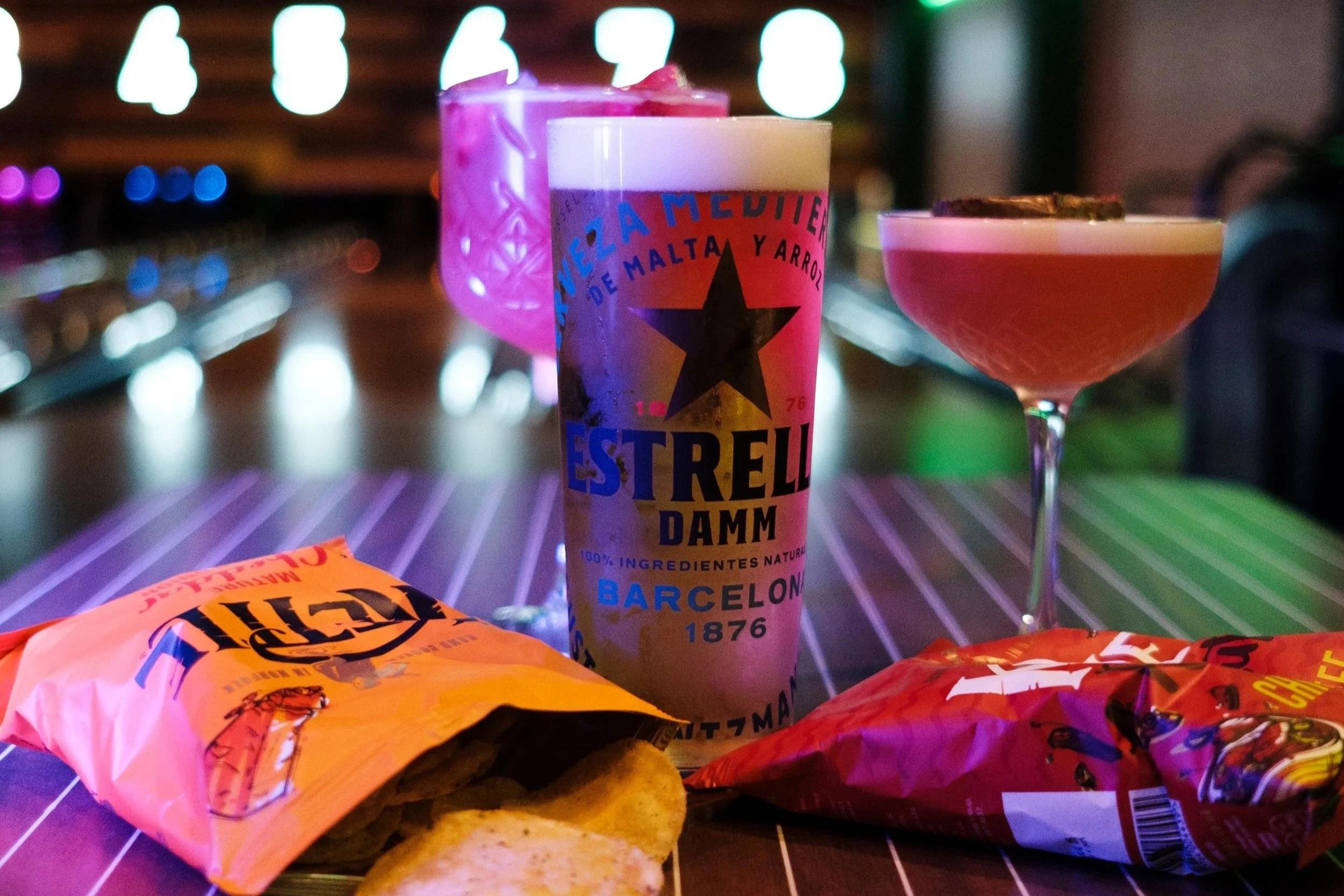 Colorful cocktails and snacks on a bar table at night with blurred neon lights in the background.