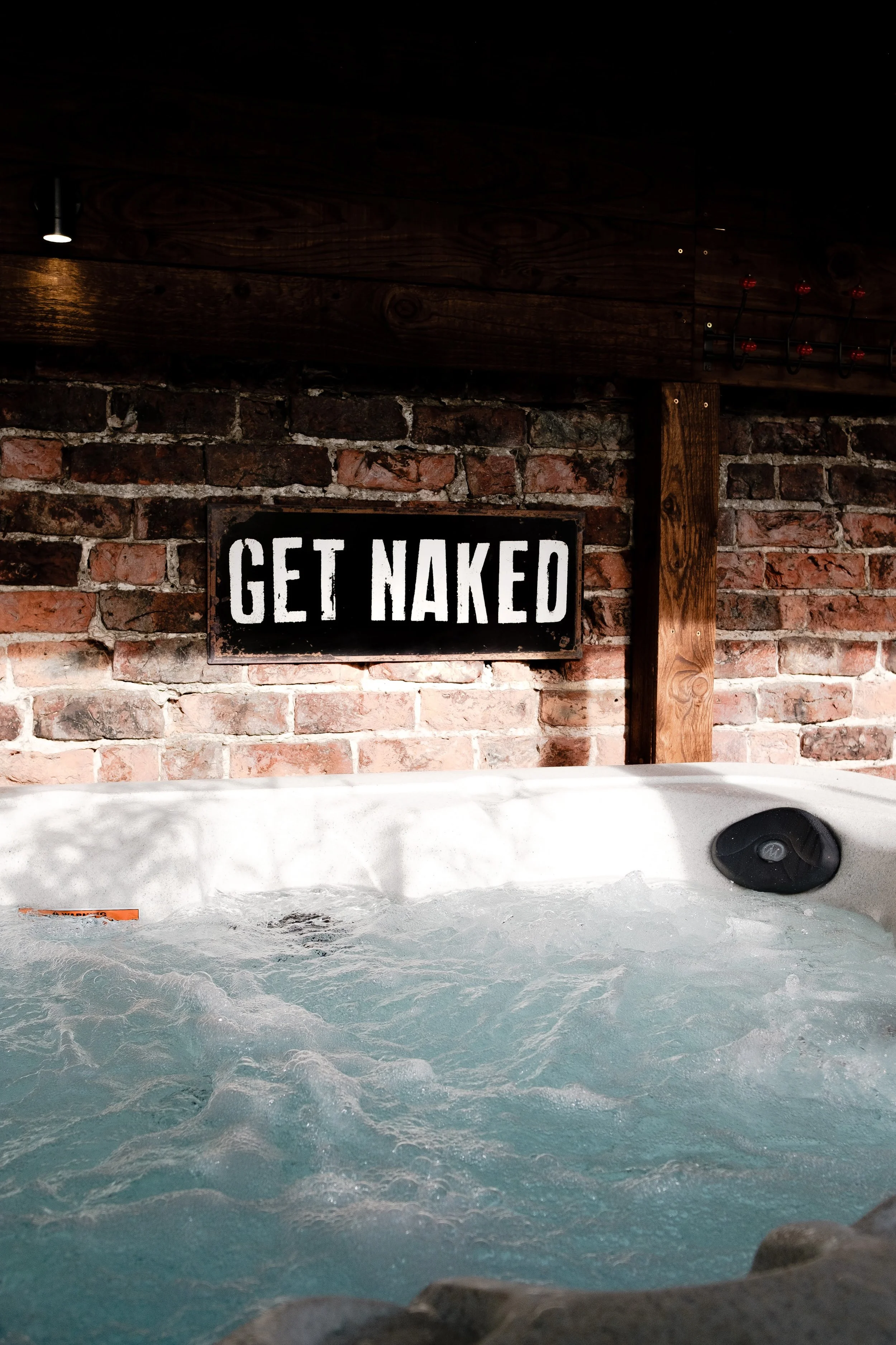 Indoor hot tub with bubbling water, brick wall, and a sign that says 'Get Naked'