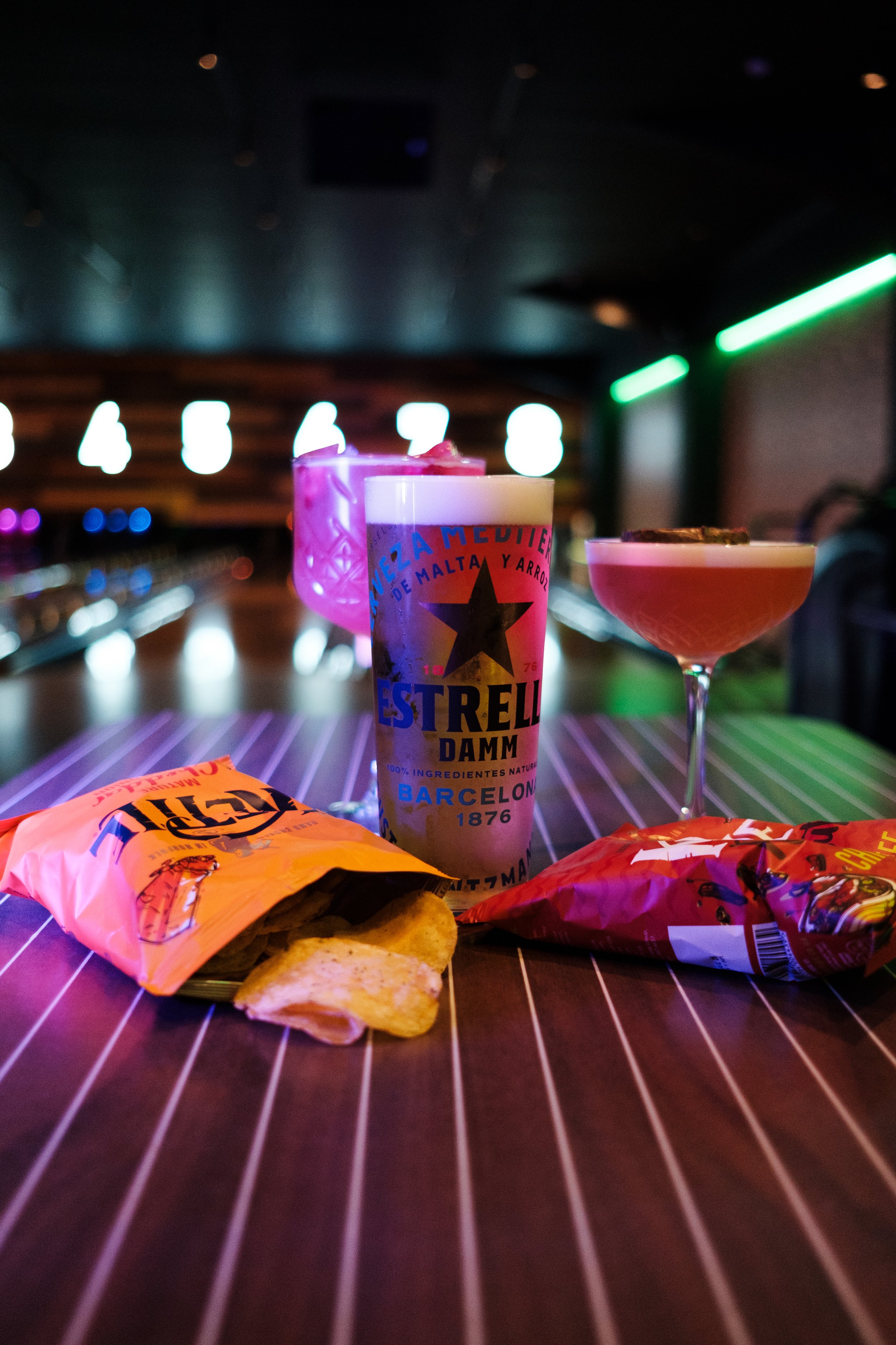 Colorful cocktails and snacks on a bar table at night with blurred neon lights in the background.