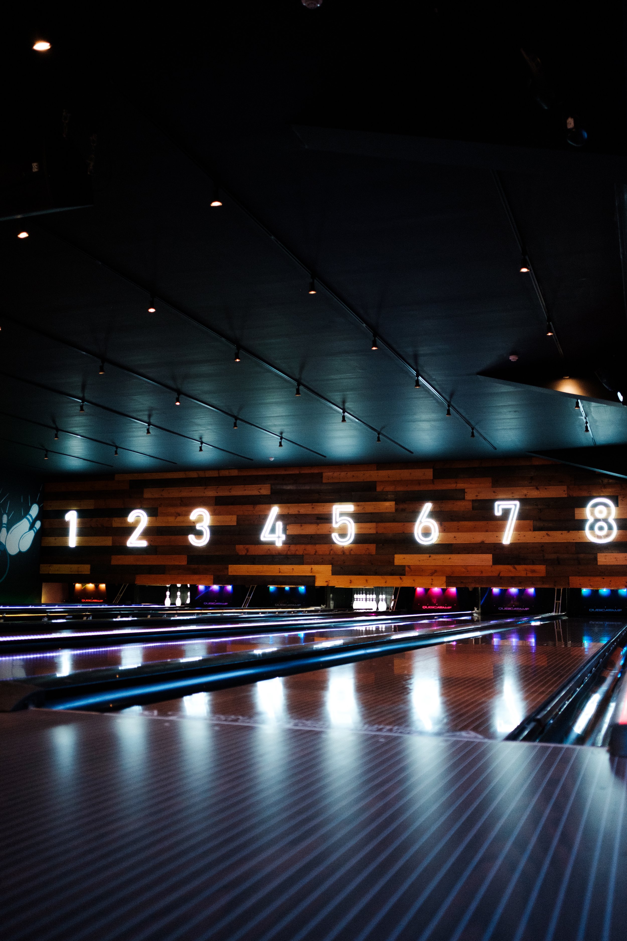 Indoor bowling alley with neon illuminated lane numbers from 1 to 8 on a wood-paneled wall.
