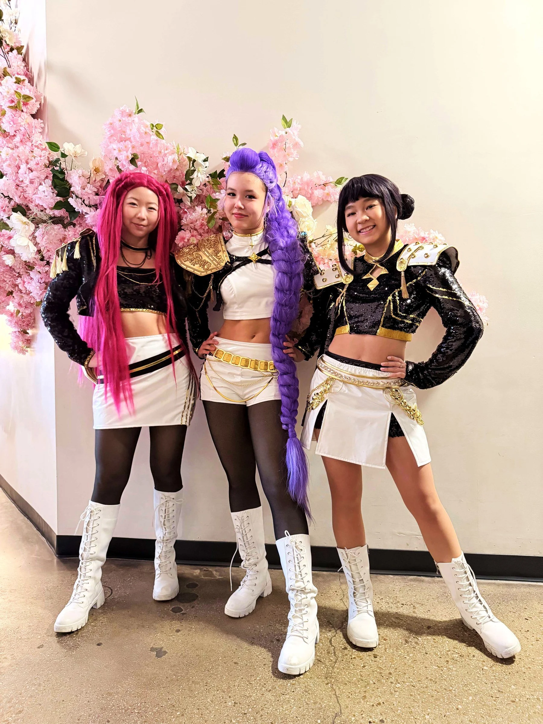 Three K-Pop stars posing in front of a flower wall at a birthday party