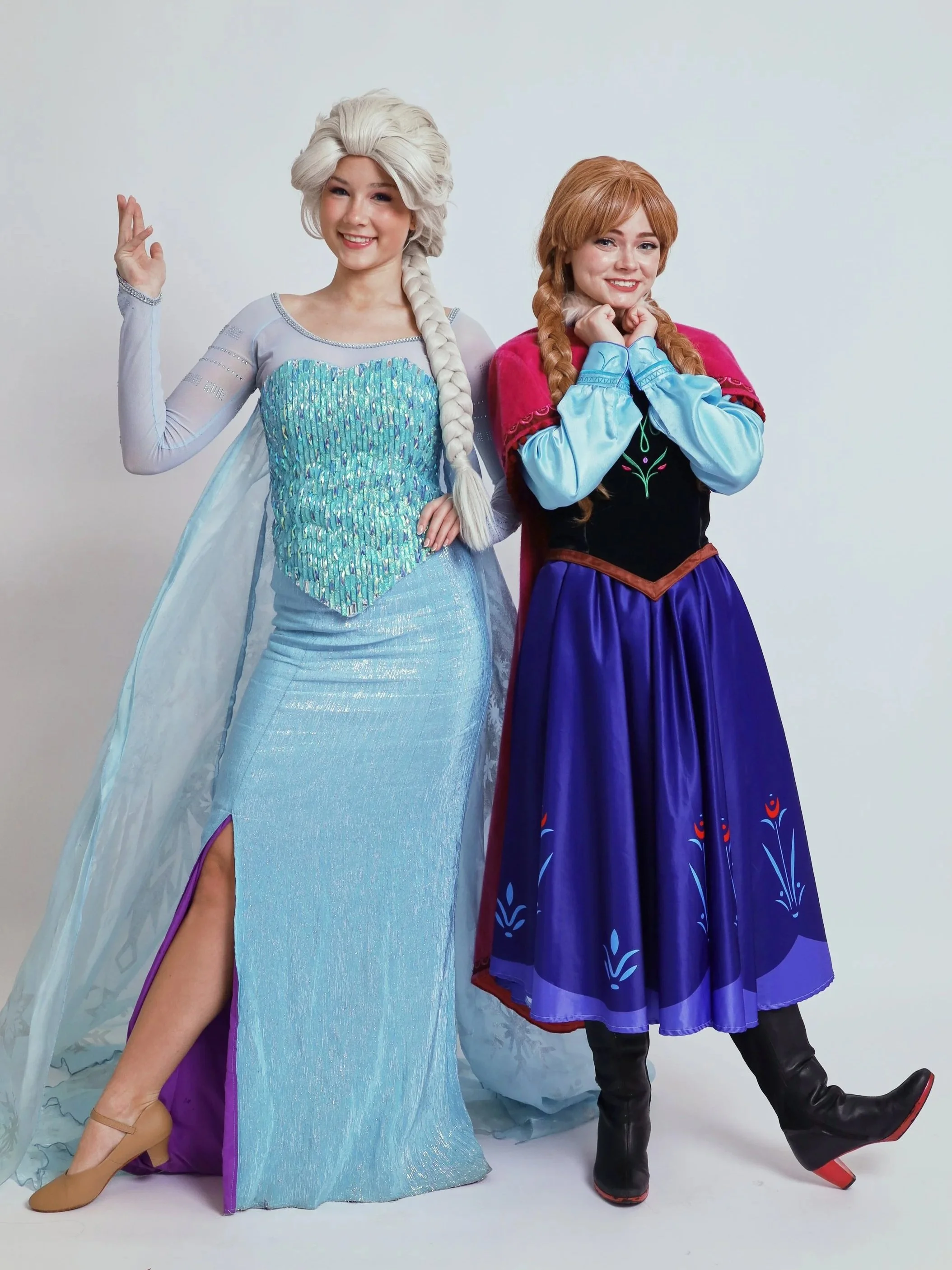 Three people in Frozen-themed costumes, including two adults dressed as popular characters with a child between them. Blue and white balloons and party decorations in the background.