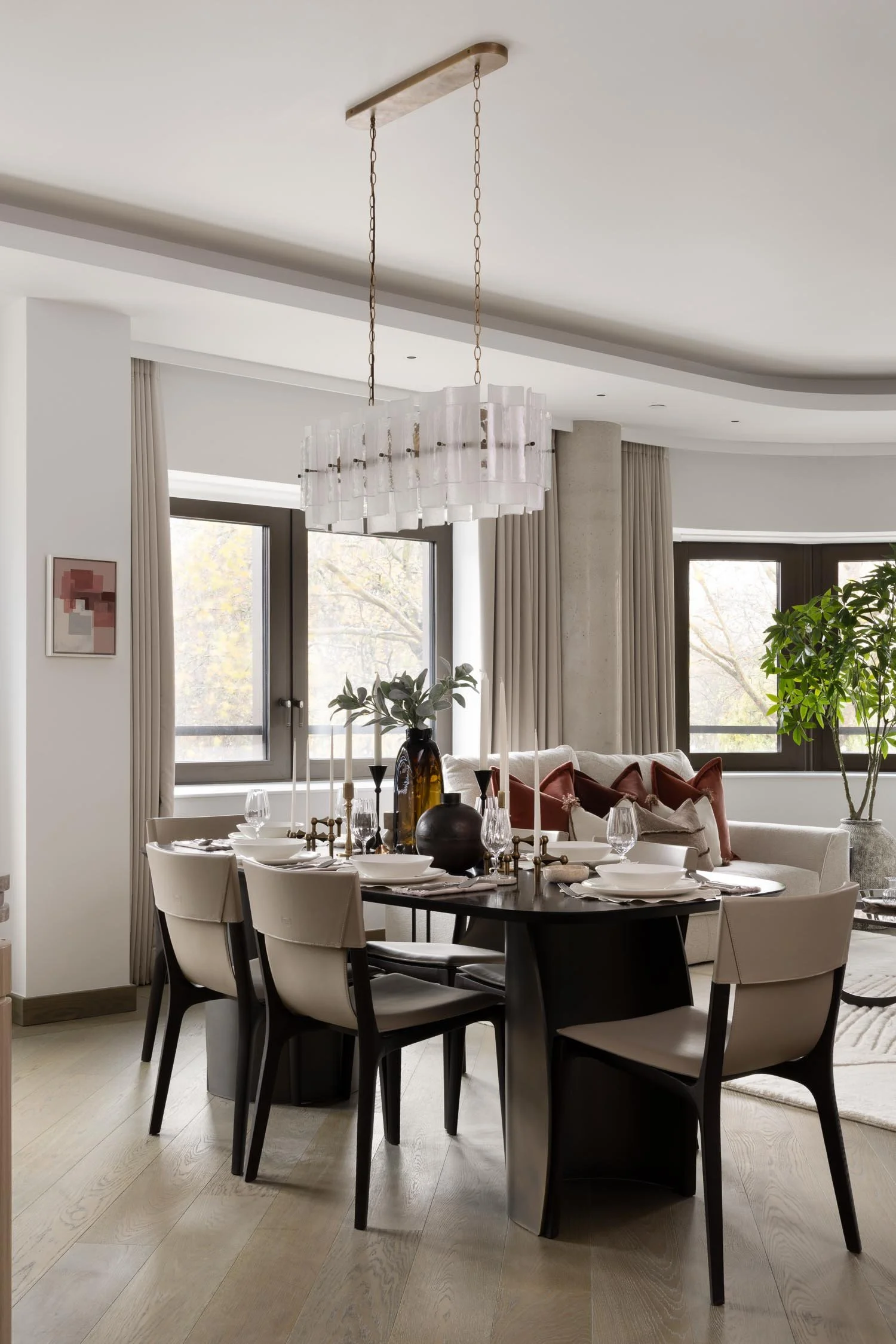 Elegant dining room with a long dark table and white chairs under a modern glass chandelier with a view of a living area