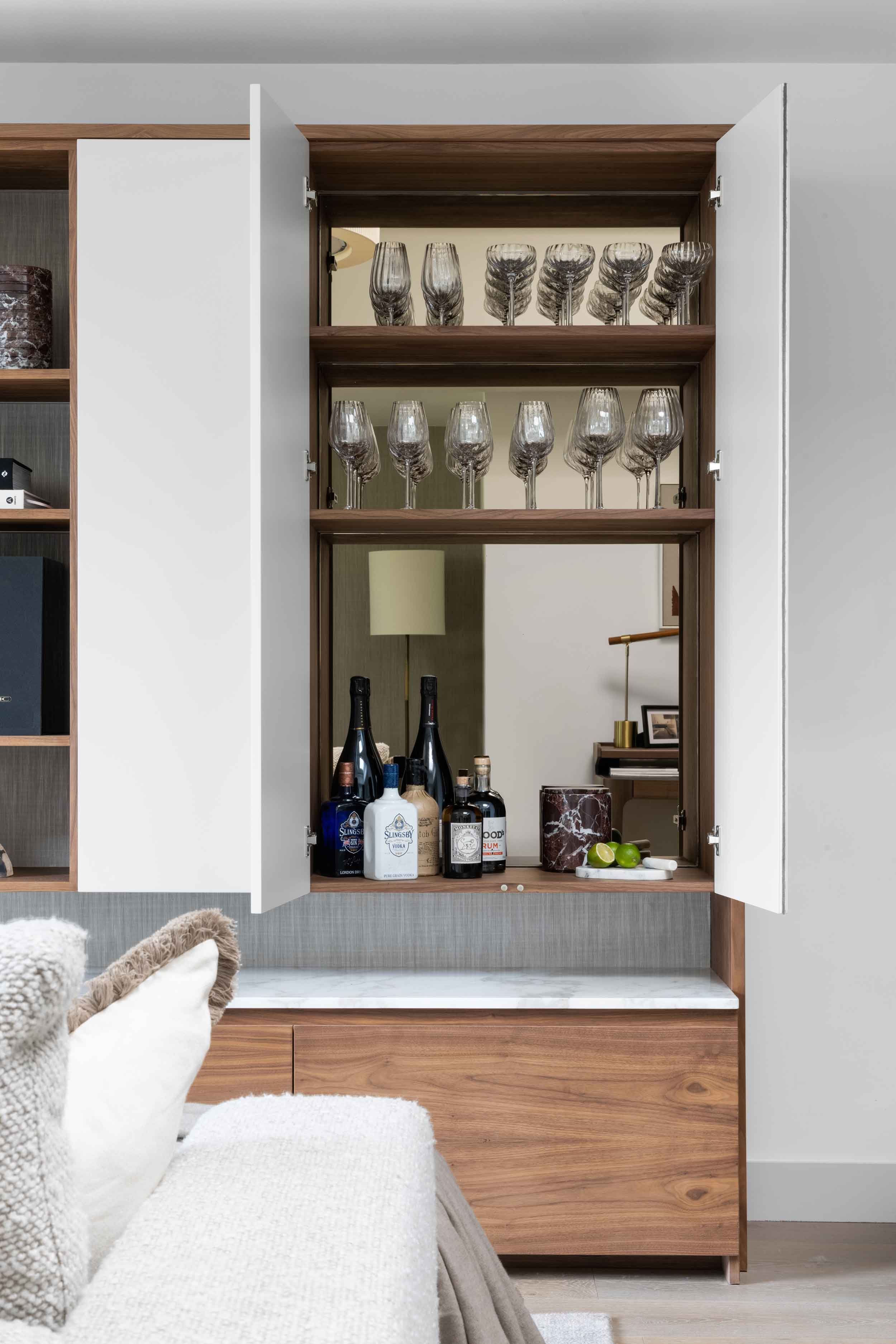  Custom cabinetry with open doors reveals a selection of modern glassware against a mirrored background in an open-plan room 