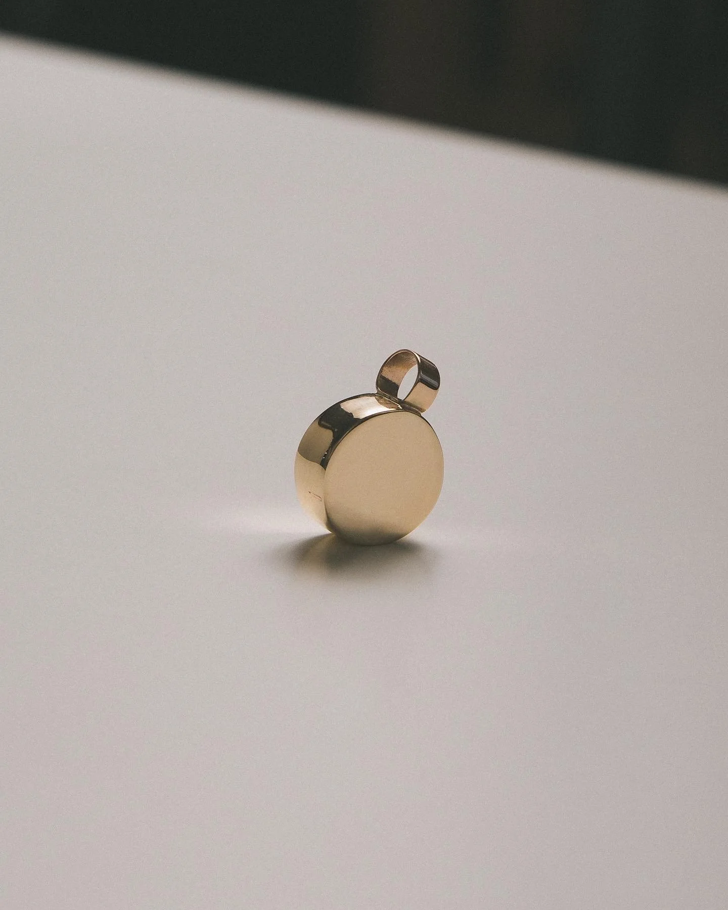 A gold-colored round keychain with a small loop on top, placed on a plain white surface.