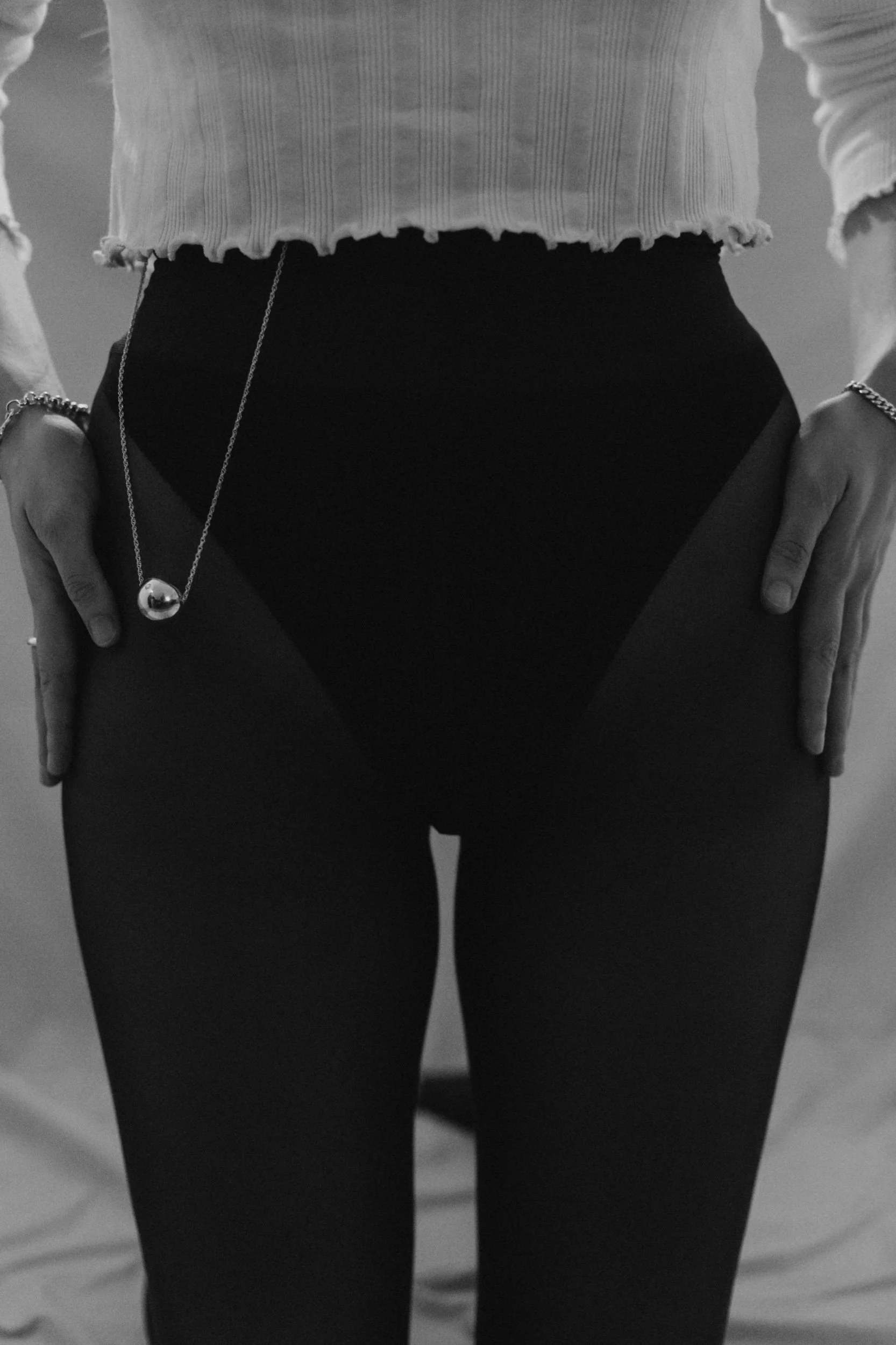Black and white image, big silver necklace tucked into the waistband of a girls tights