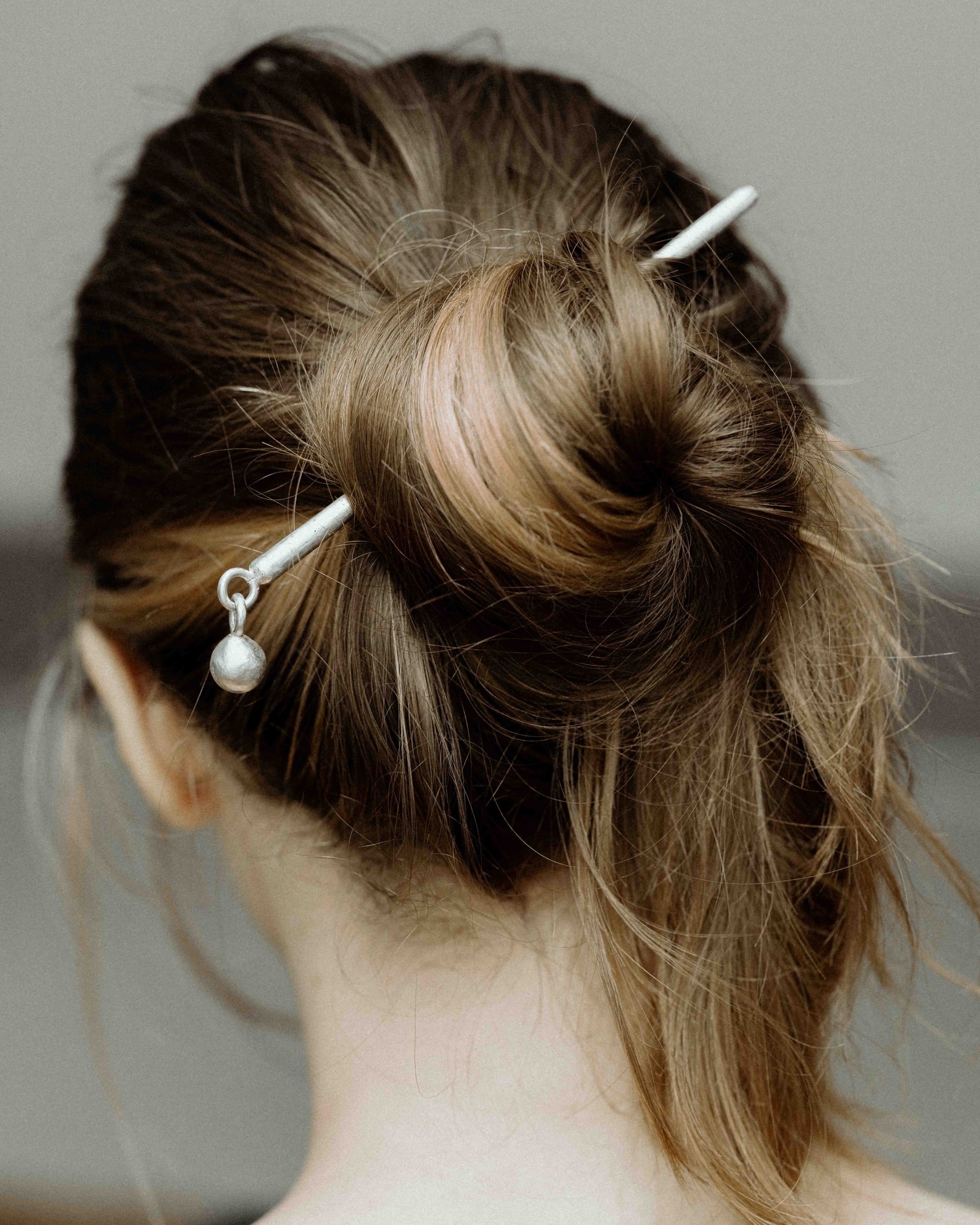 Close-up of a womans brunette and blond hair knotted into a bun, held with a sterling silver hair stick.
