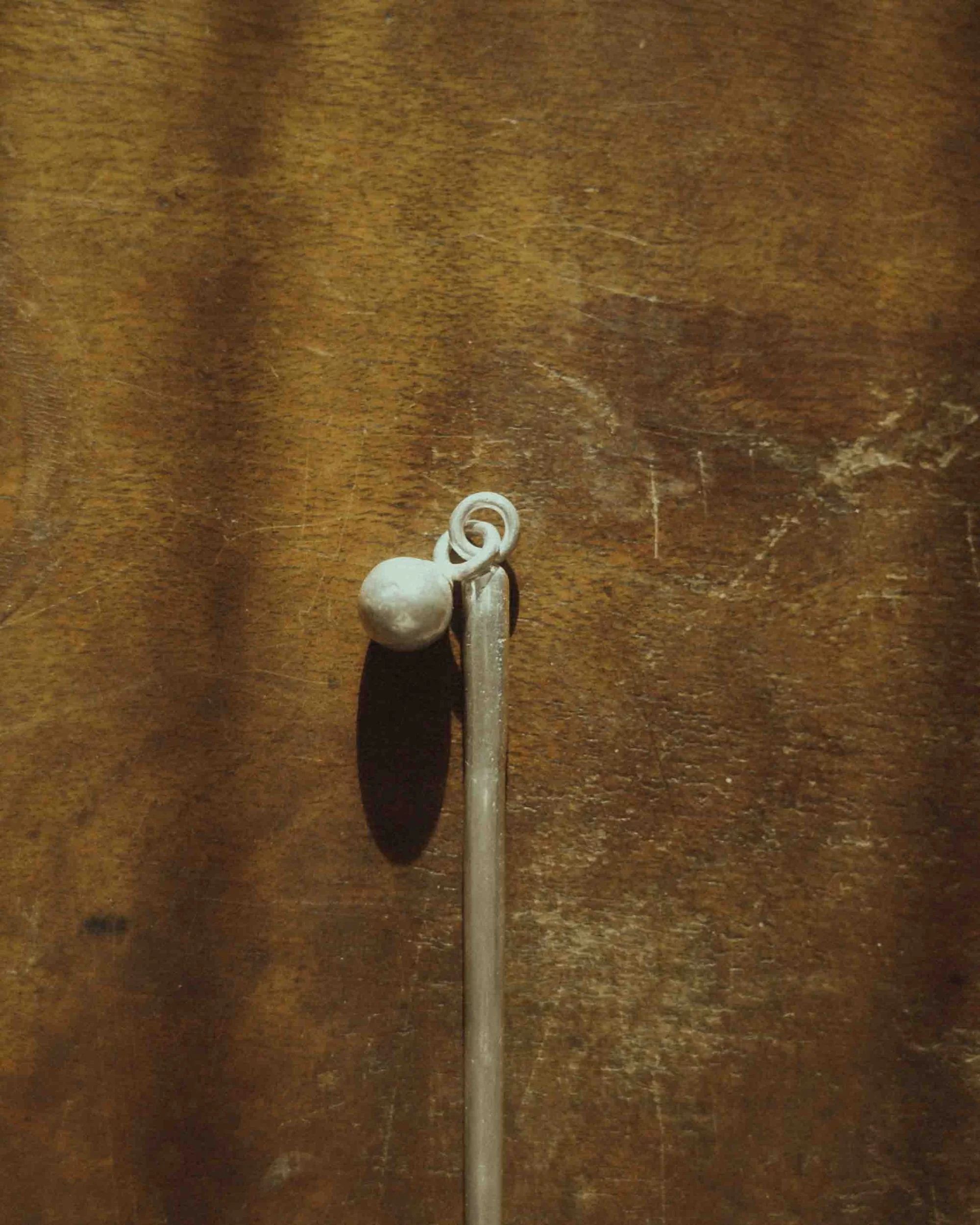 a close up of a sterling silver hair stick, placed on a wooden surface.