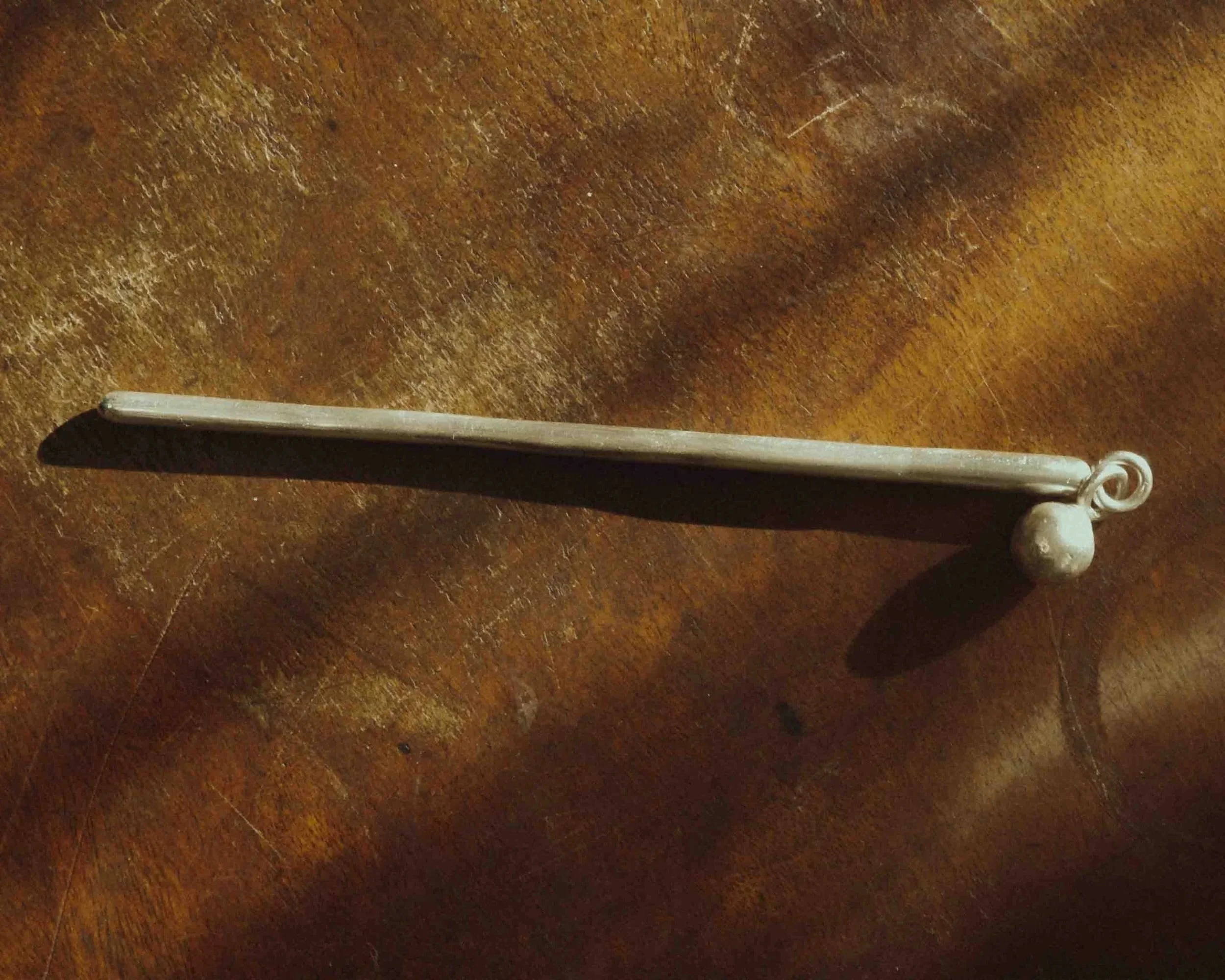 a sterling silver hair stick placed on a wooden surface.