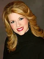 Portrait of a smiling person with long, wavy hair wearing a black turtleneck.