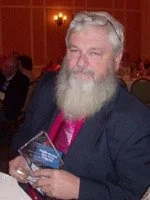 A bearded man in a suit holding an award at an event.
