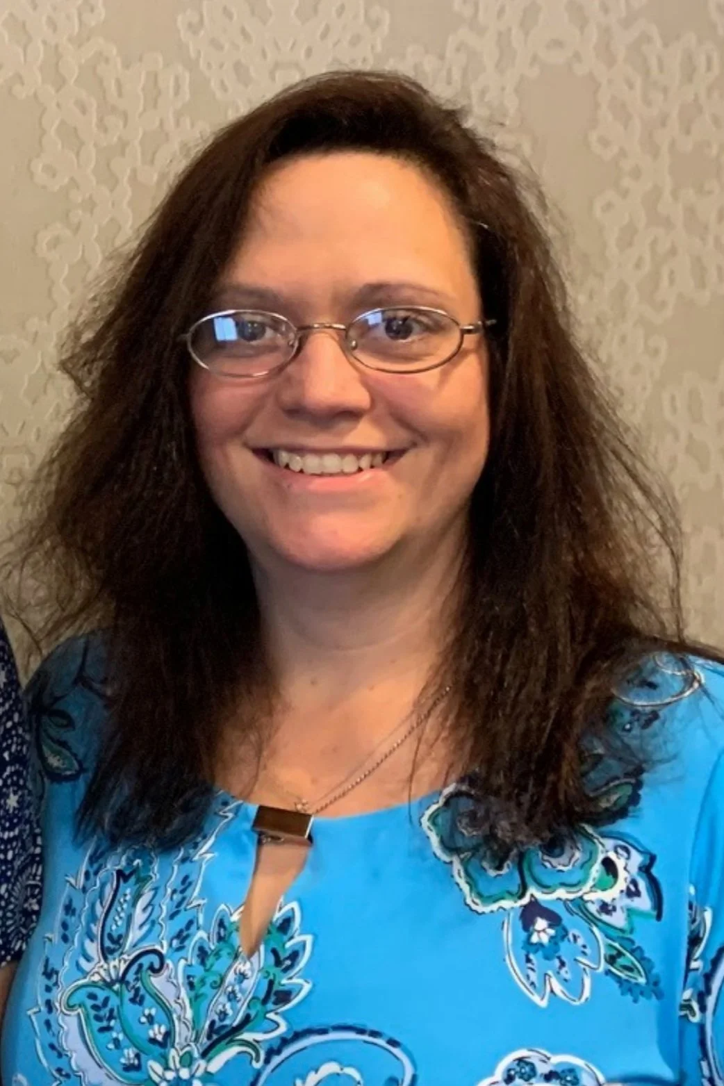 A woman wearing glasses and a blue floral-patterned shirt smiling.