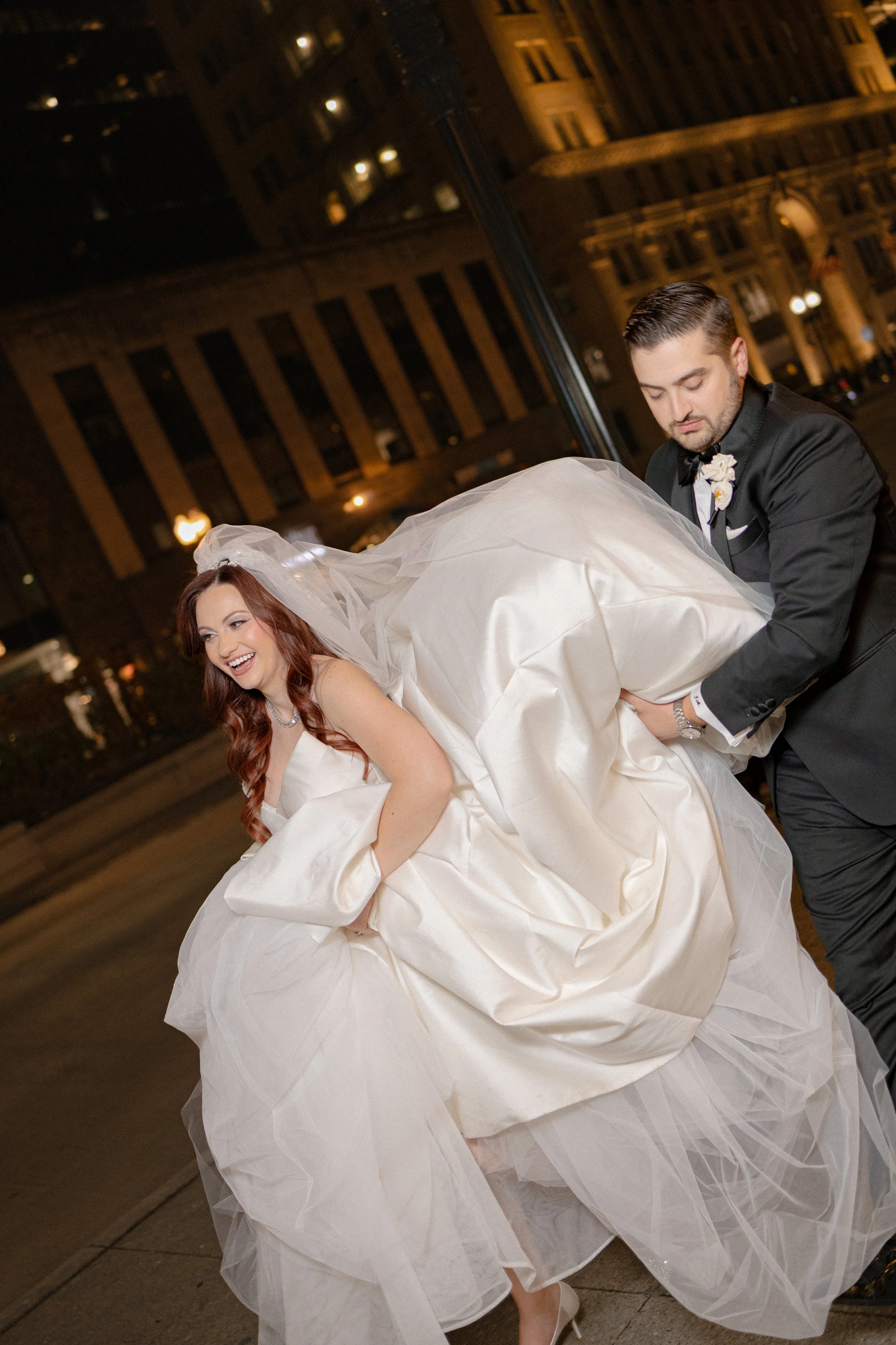 A bride and groom sharing an intimate moment at sunset, framed by tall white columns and a large green tree in the background.