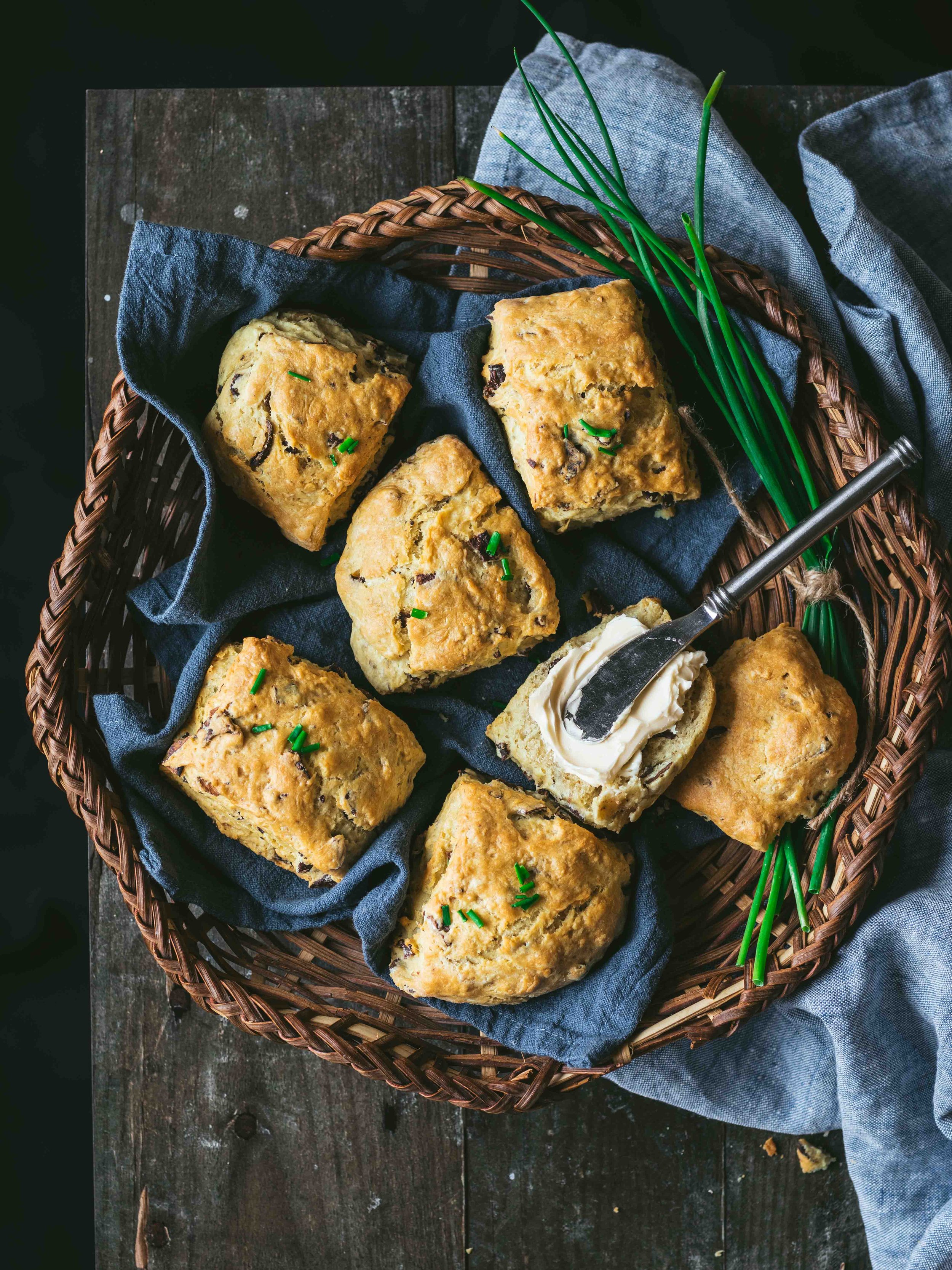MyBacon Biscuits in a basket with a blue cloth napkin. One biscuit has vegan butter ontop with a silver butterknife