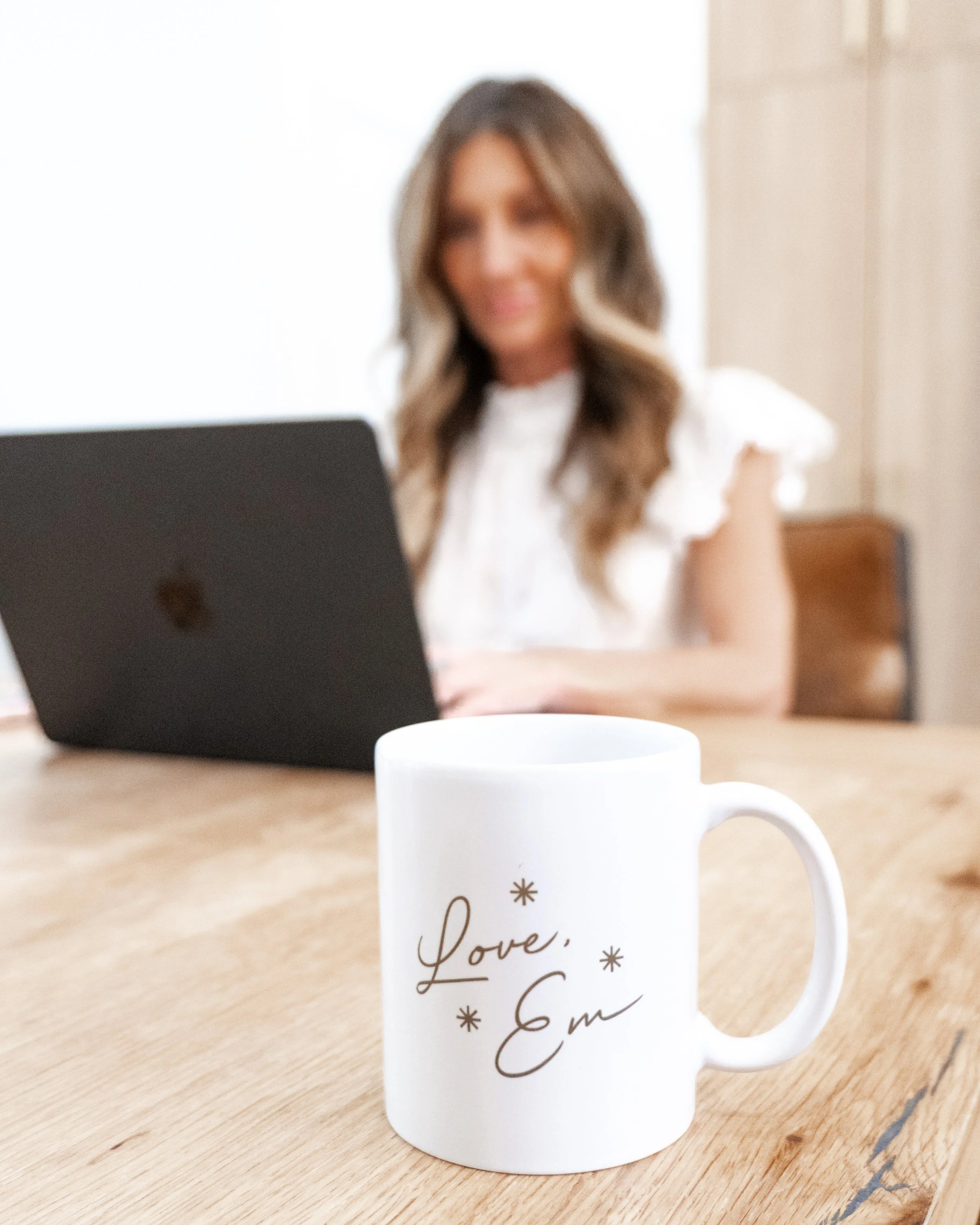 A white ceramic mug on a wooden table with black text that reads 'Love, Gm' and small decorative snowflakes around the text.