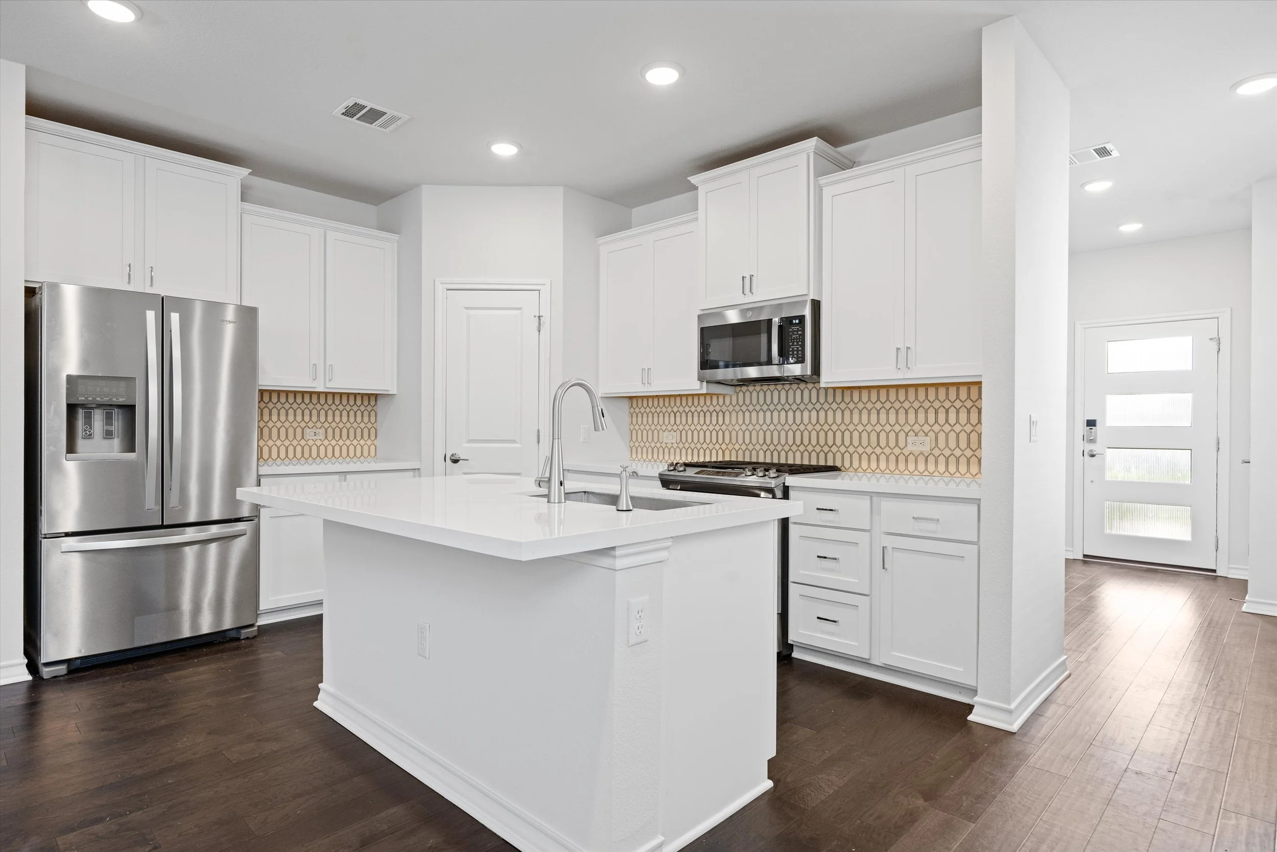 Open kitchen with white shaker cabinets, quartz center island, stainless steel appliances, gold geometric tile backsplash, and dark hardwood floors at 15604 Ellinger Dr, Austin TX 78728.