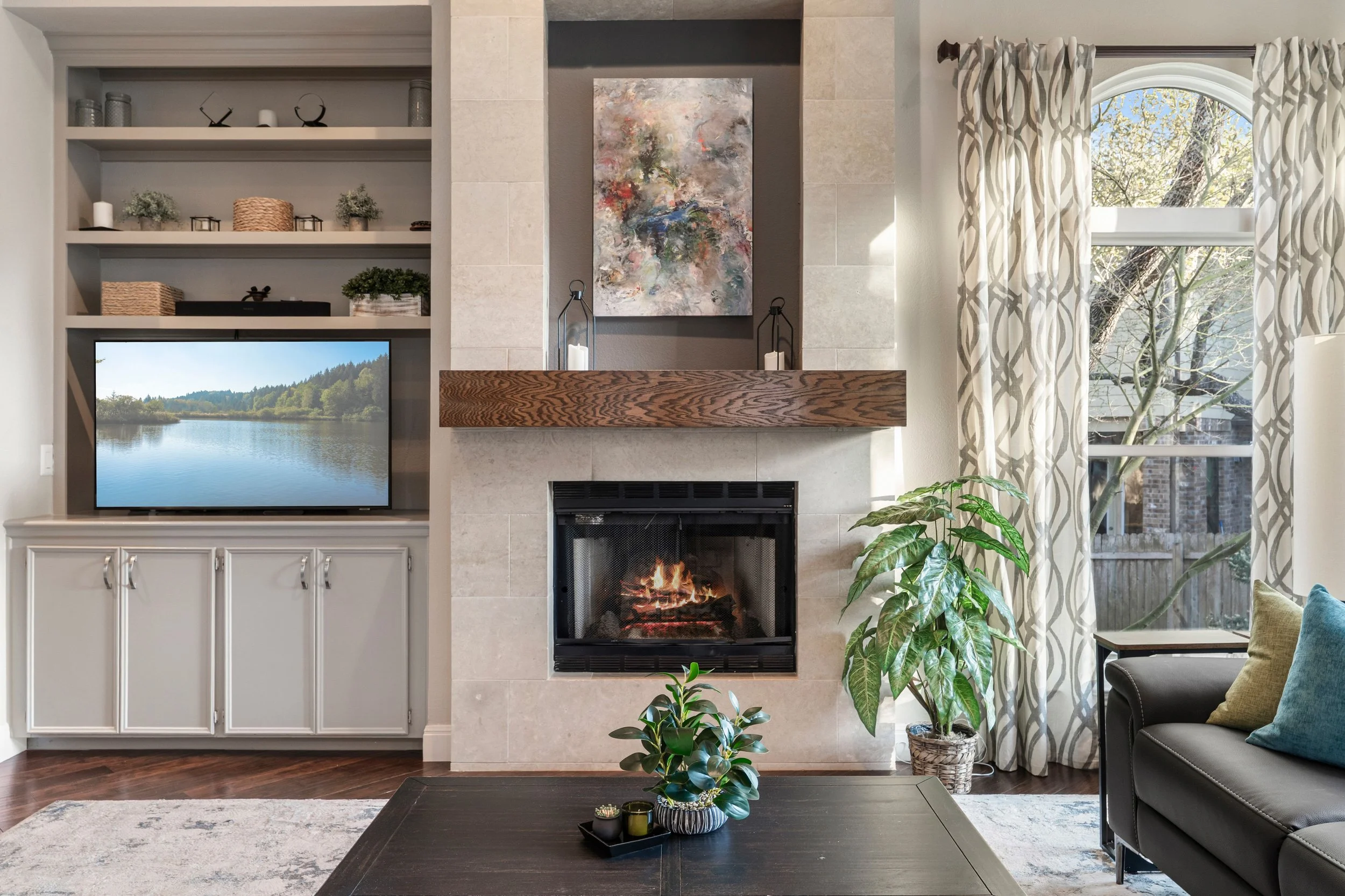 Living room with travertine fireplace, wood beam mantle, built-in shelving with TV, hardwood floors, and arched window in Circle C Ranch home at 6913 Auckland Dr, Austin TX.
