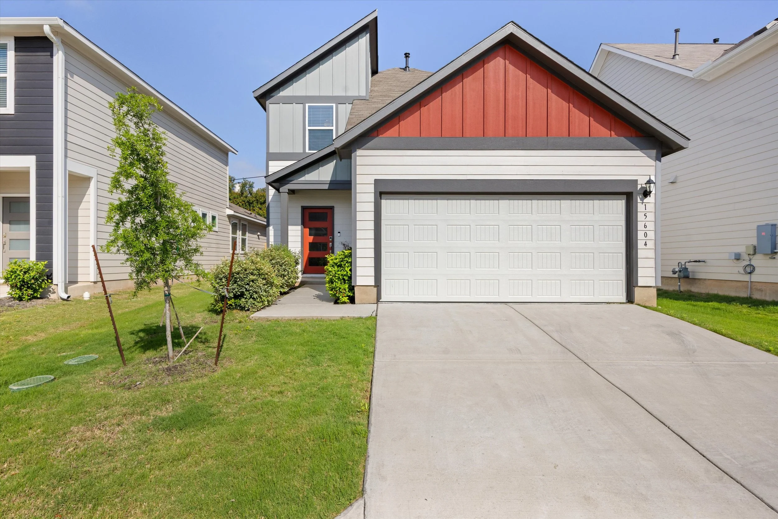 wo-story home for sale at 15604 Ellinger Dr Austin TX featuring board and batten exterior, red accent gable, bold red front door, two-car garage, and established lawn.