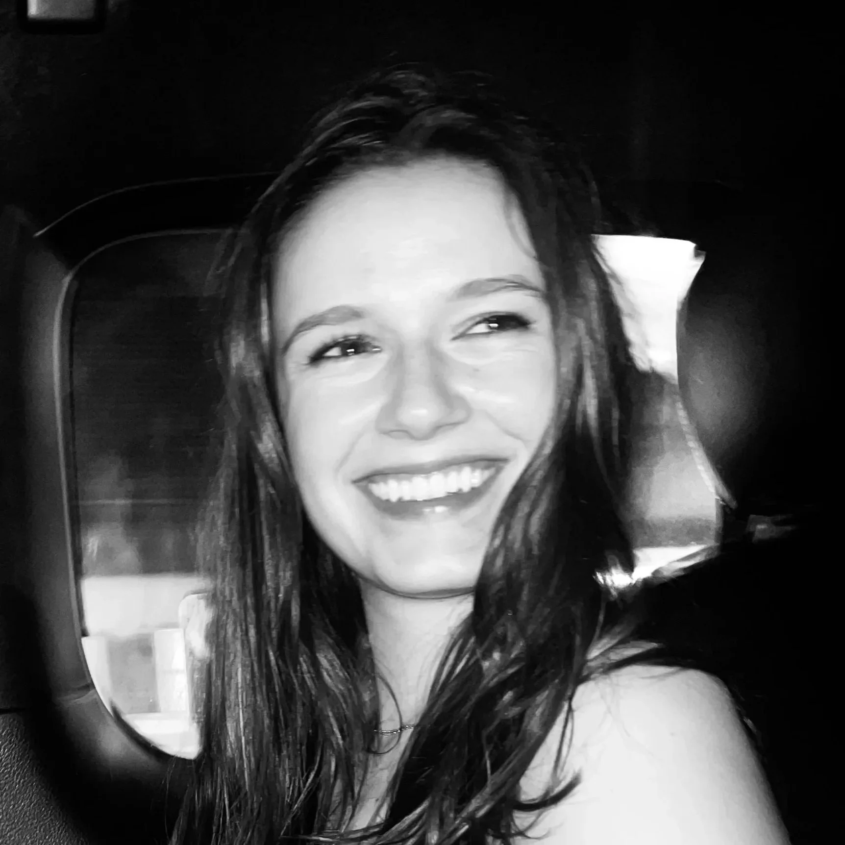 Black and white photo of a woman smiling with her hair falling over her face, partially visible in a mirror.