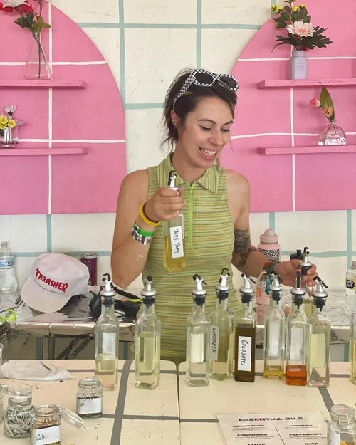 Woman smiling and pouring essential oils into bottles at a colorful shop display