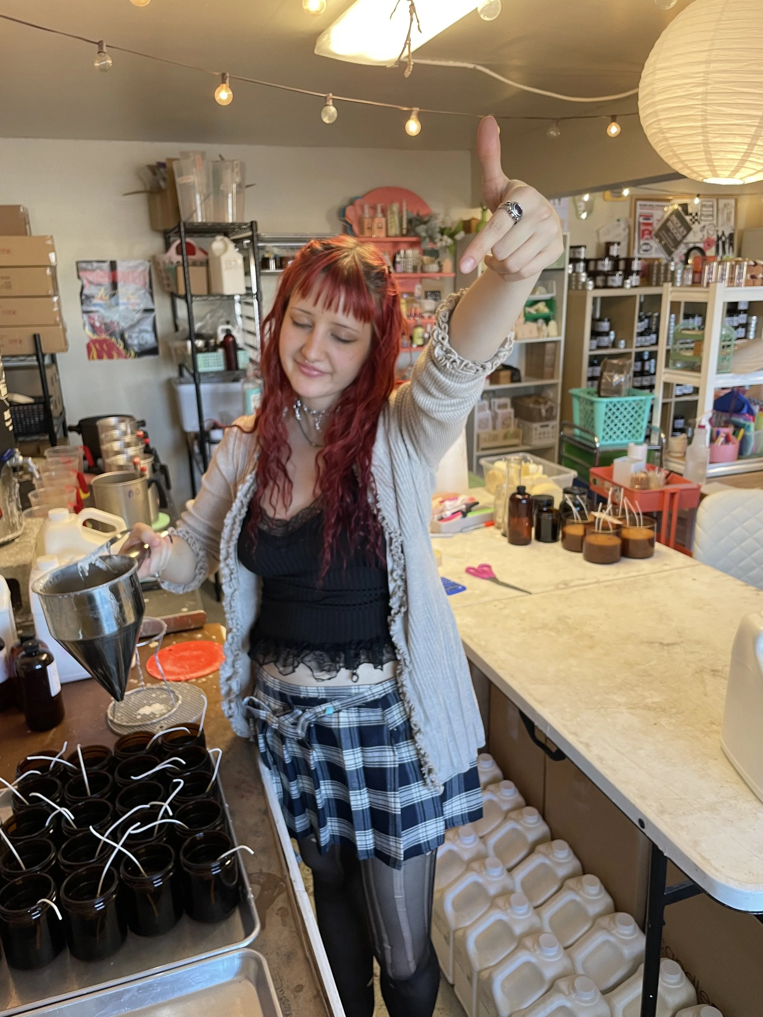 A young boy with glasses smiling outdoors at a park, wearing a yellow T-shirt, purple patterned shorts, and a black and purple jacket, with a chain-link fence and palm trees in the background.