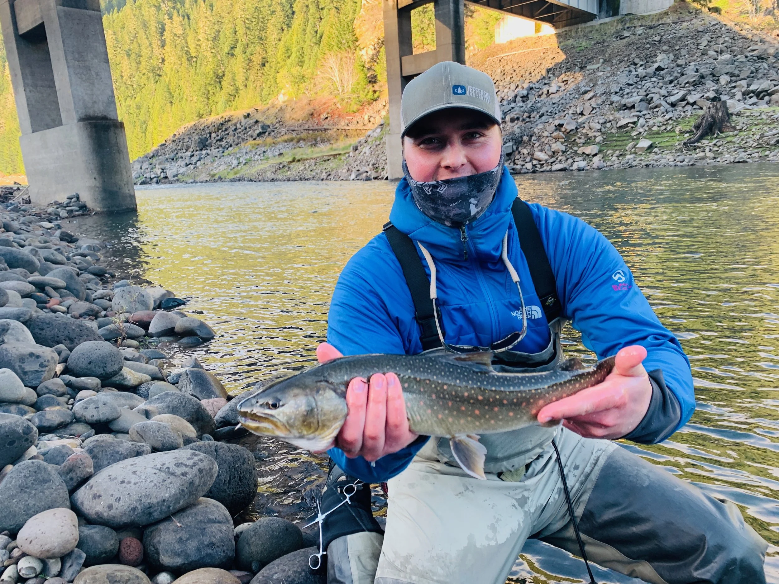 Person holding a fish by a river under a bridge