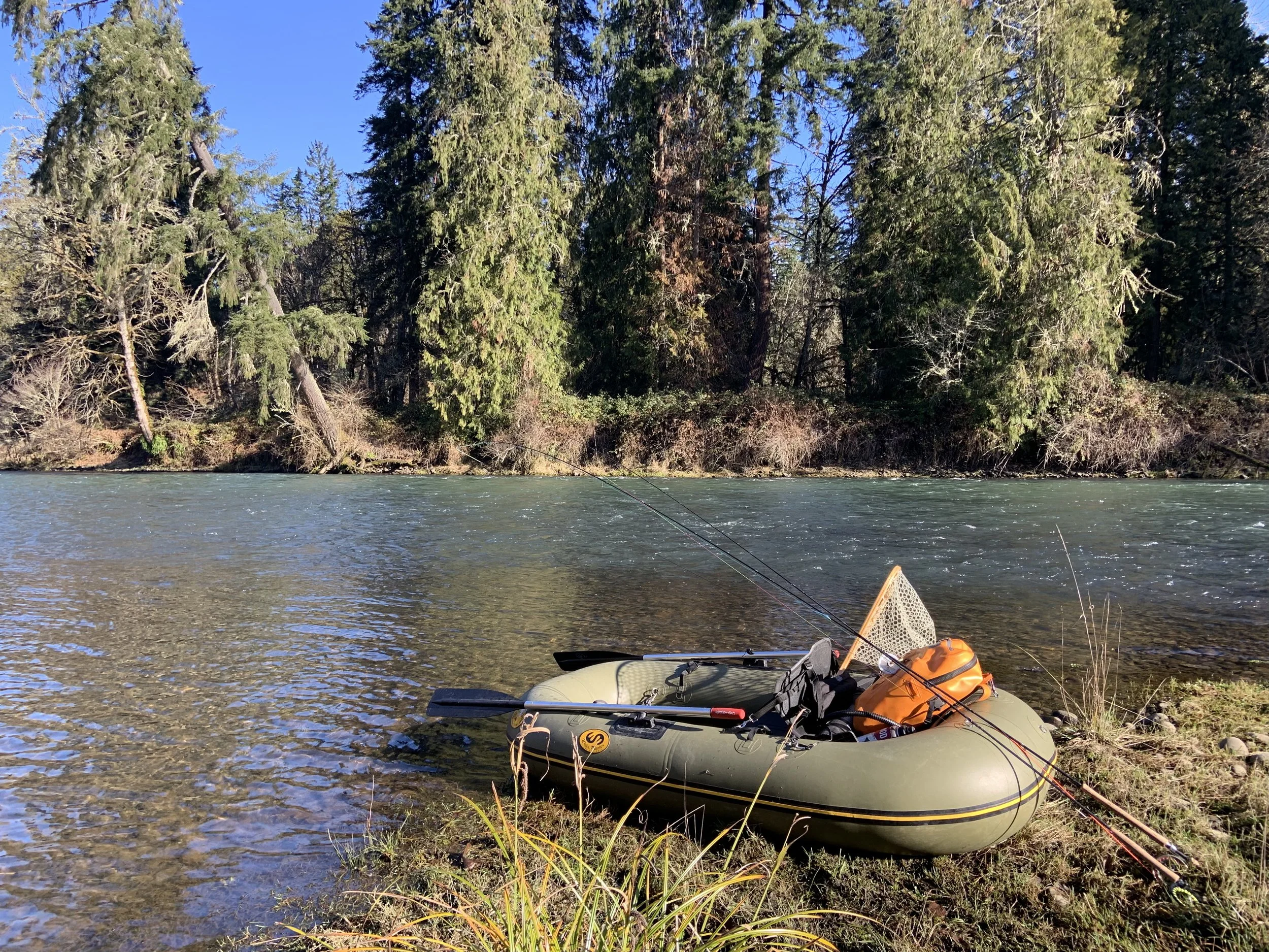 Inflatable fishing raft on riverbank surrounded by trees and water