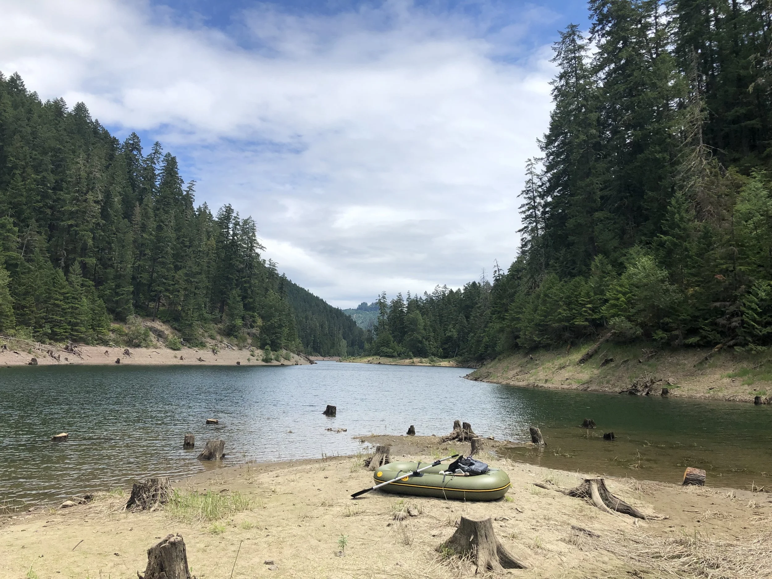 Inflatable boat on a lake shore surrounded by dense forest