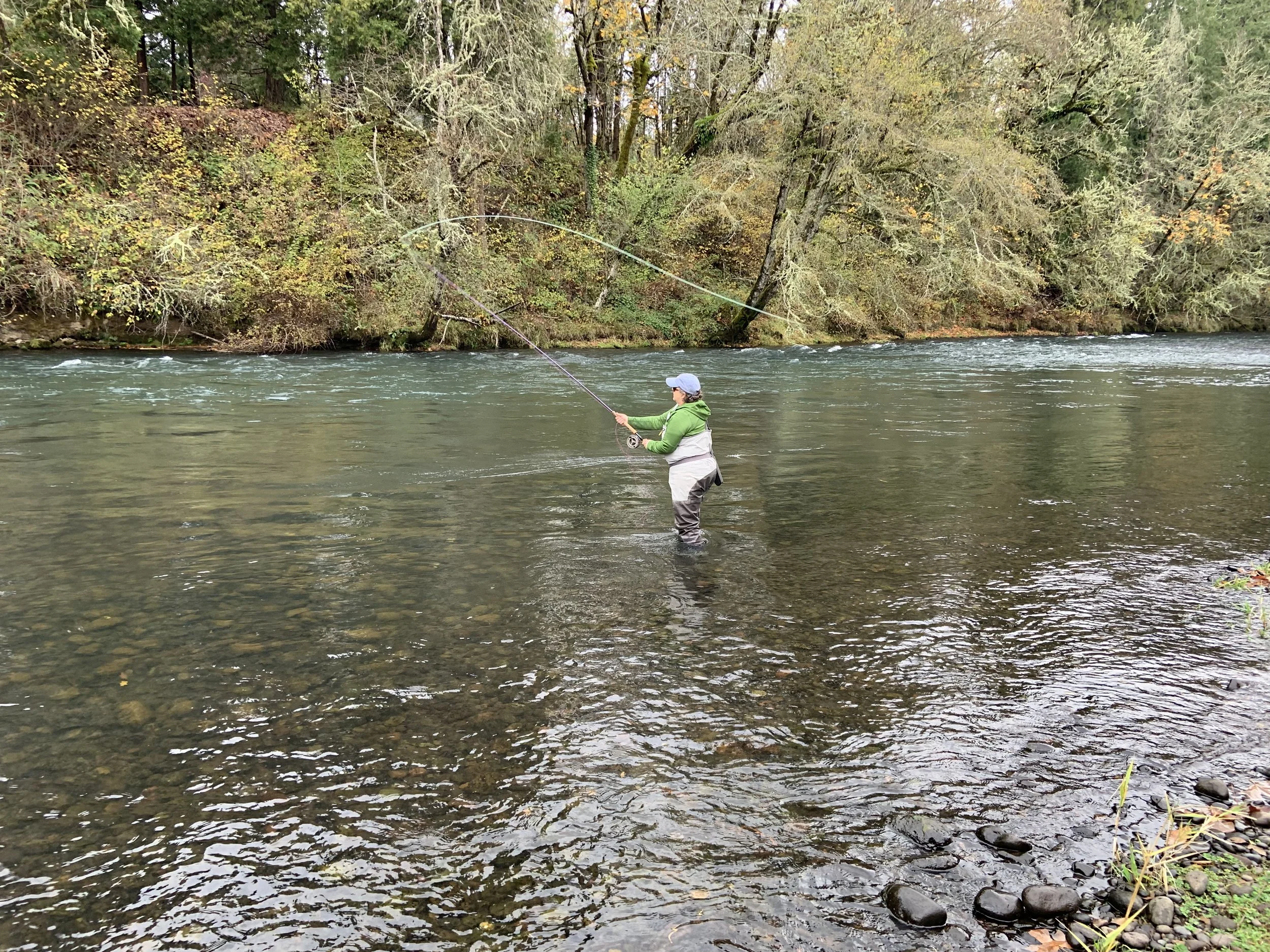 Person fly fishing in a river surrounded by trees.