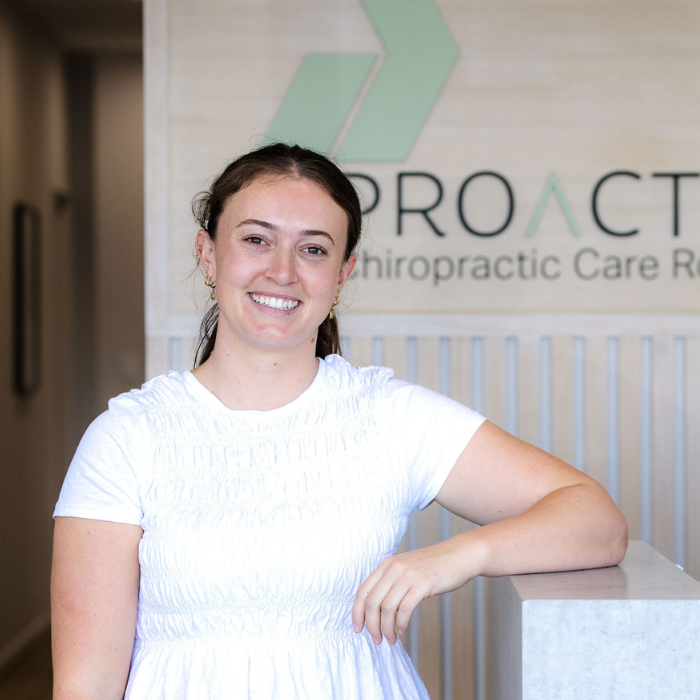 Smiling woman with short brown hair wearing a striped cream and black sweater outdoors with trees and plants in the background.